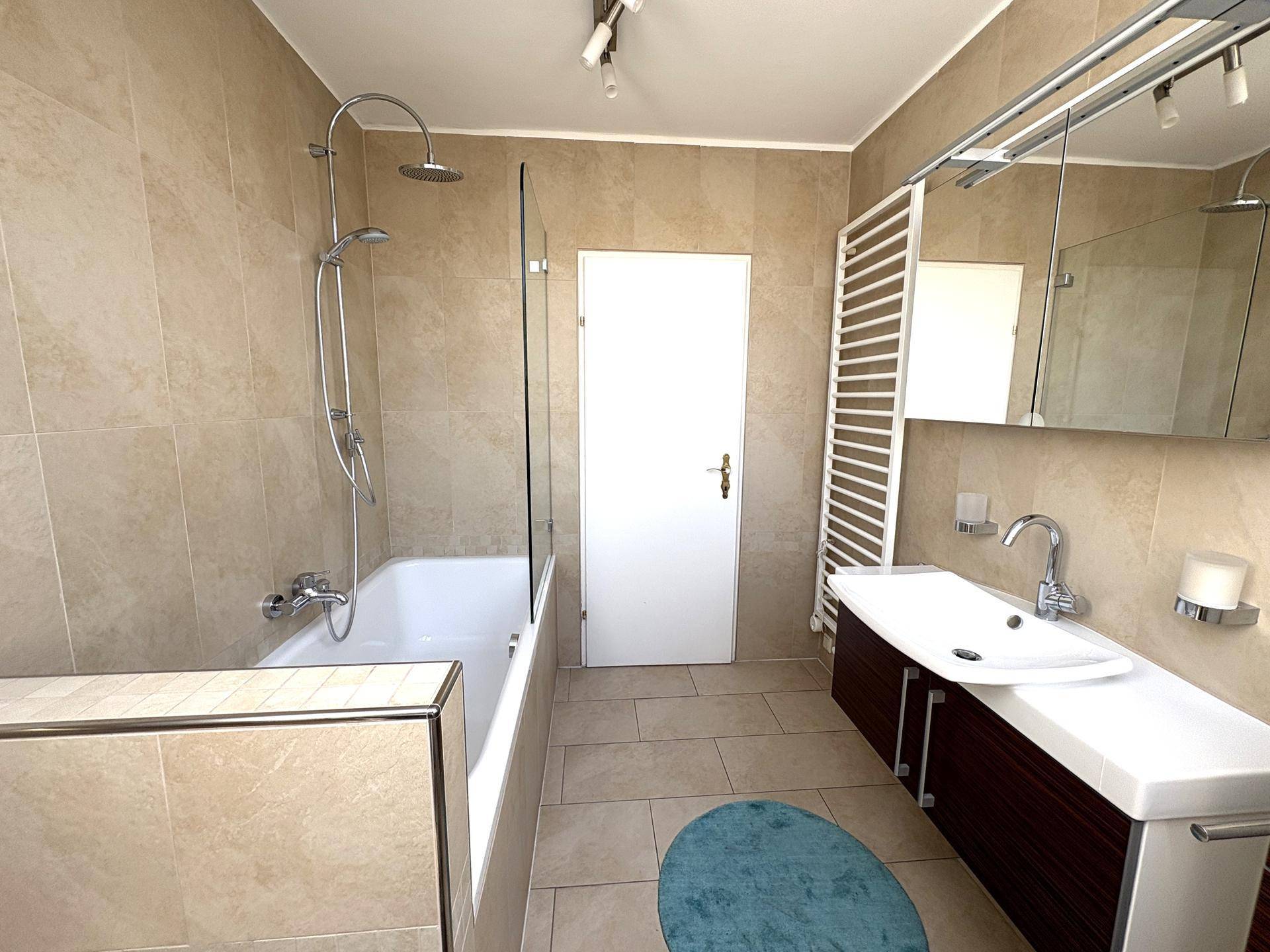 Helles Badezimmer mit Badewanne, Duschfunktion und modernem Waschtisch, ausgestattet mit Handtuchheizkörper.