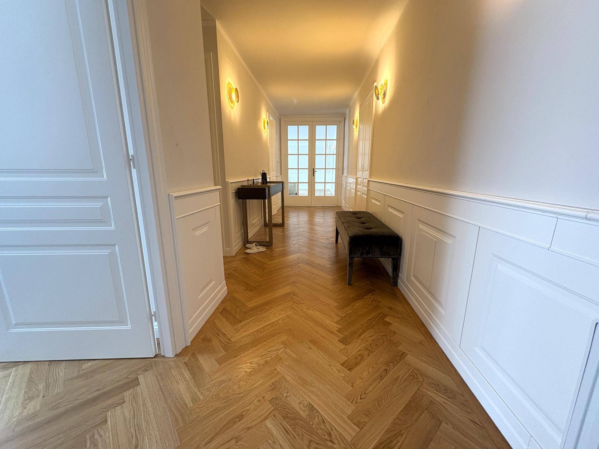 Eleganter Flur mit Fischgrätparkett, Wandpaneelen und stilvollen Wandleuchten.