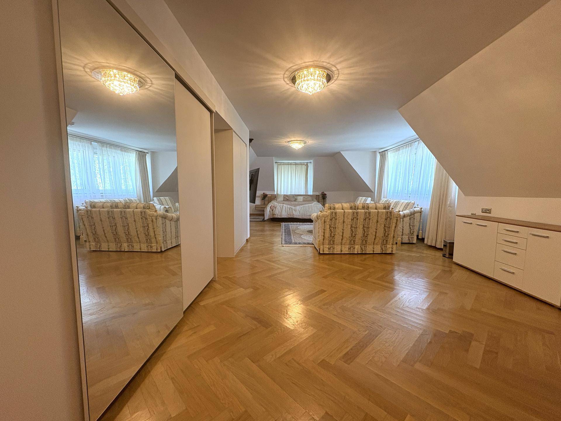 Großes Dachgeschosszimmer mit Fischgrätparkett, gemütlichen Sofas und Spiegelschränken, ideal als Schlaf- und Wohnbereich.