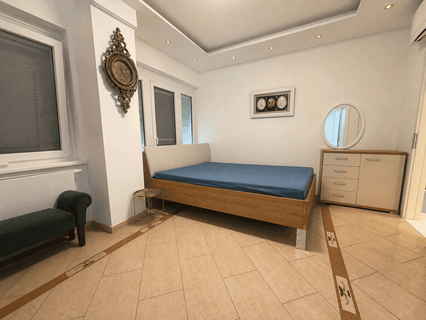 Helles Schlafzimmer mit Doppelbett, Kommode und Fliesenboden.