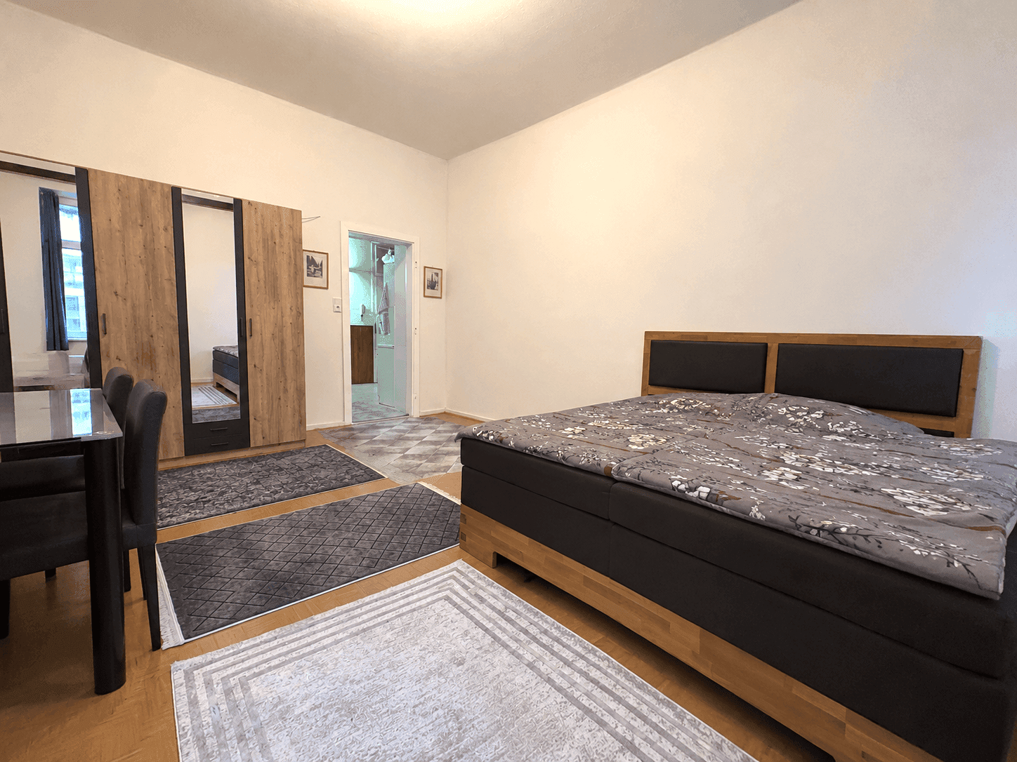 Schlafzimmer mit großem Doppelbett, Kleiderschrank mit Spiegeltüren und Zugang zu einem weiteren Raum.
