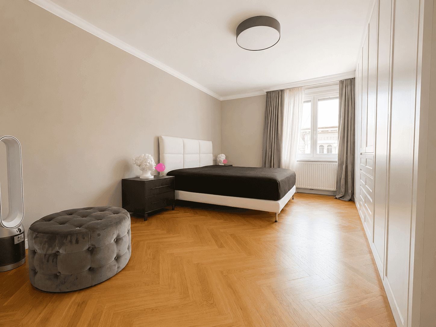 Helles Schlafzimmer mit großem Bett, weißen Einbauschränken und elegantem Fischgrätparkett.