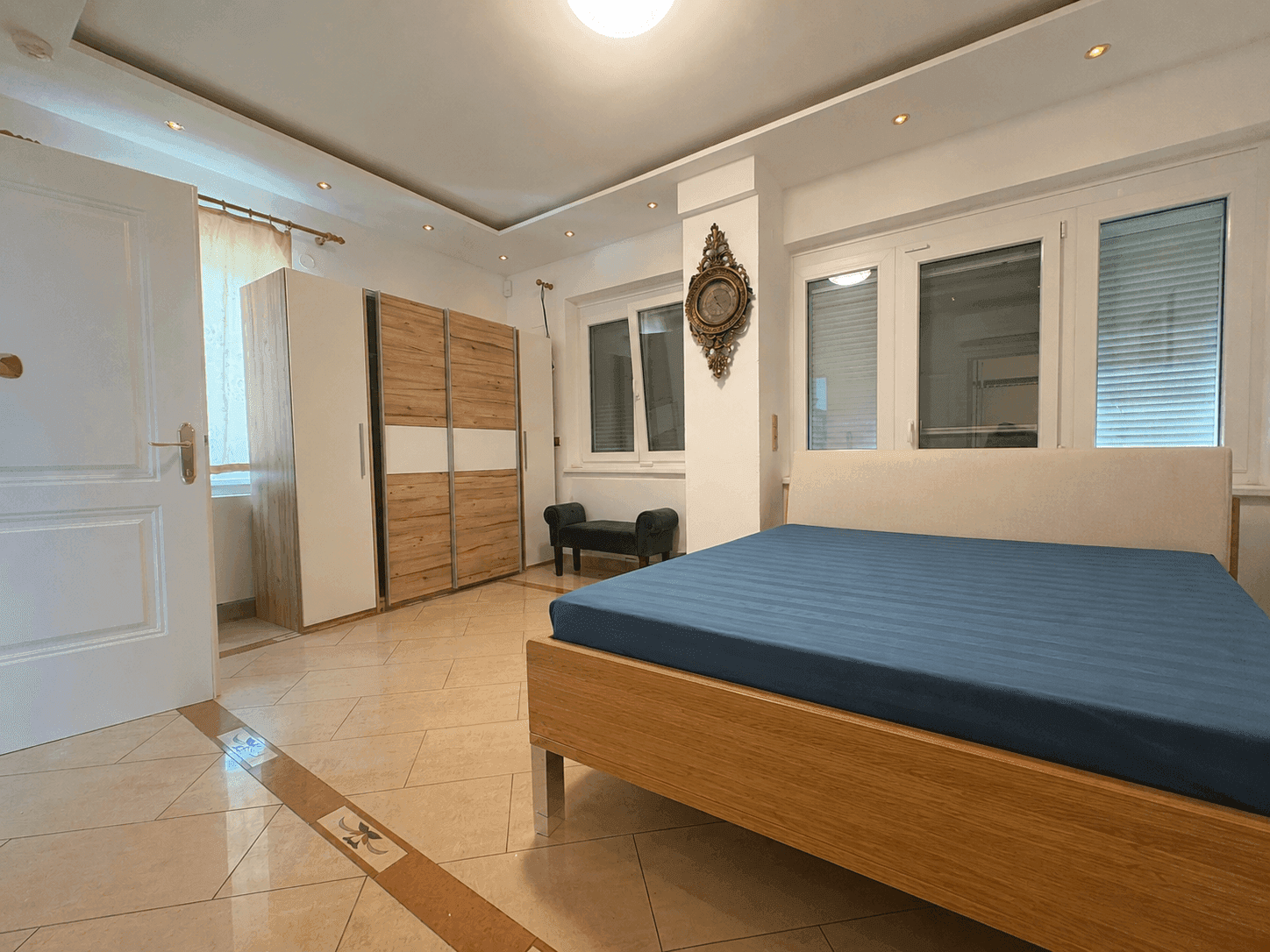 Geräumiges Schlafzimmer mit Bett, Kleiderschrank und großen Fenstern.