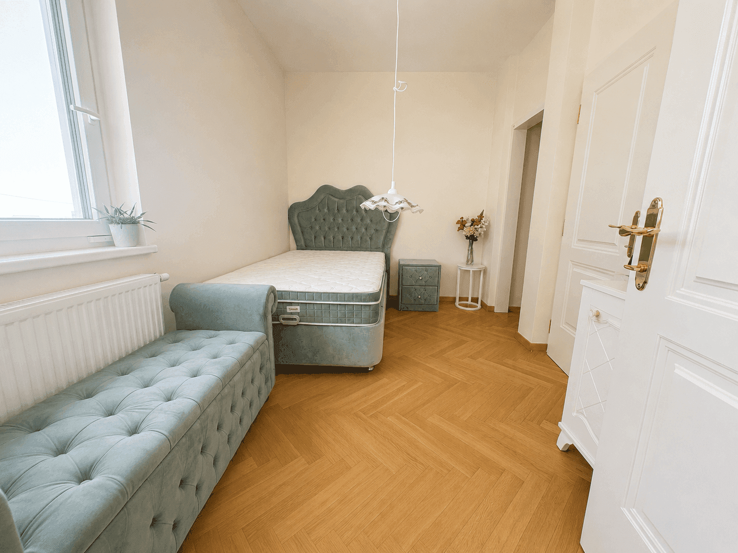 Gemütliches Schlafzimmer mit Einzelbett, Sitzbank und elegantem Fischgrätparkett, bietet eine ruhige Atmosphäre.