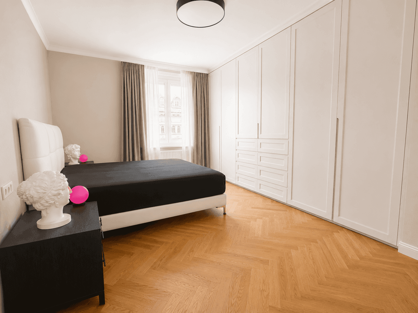 Geräumiges Schlafzimmer mit weißen Einbauschränken, großem Bett und hellem Fischgrätparkett.