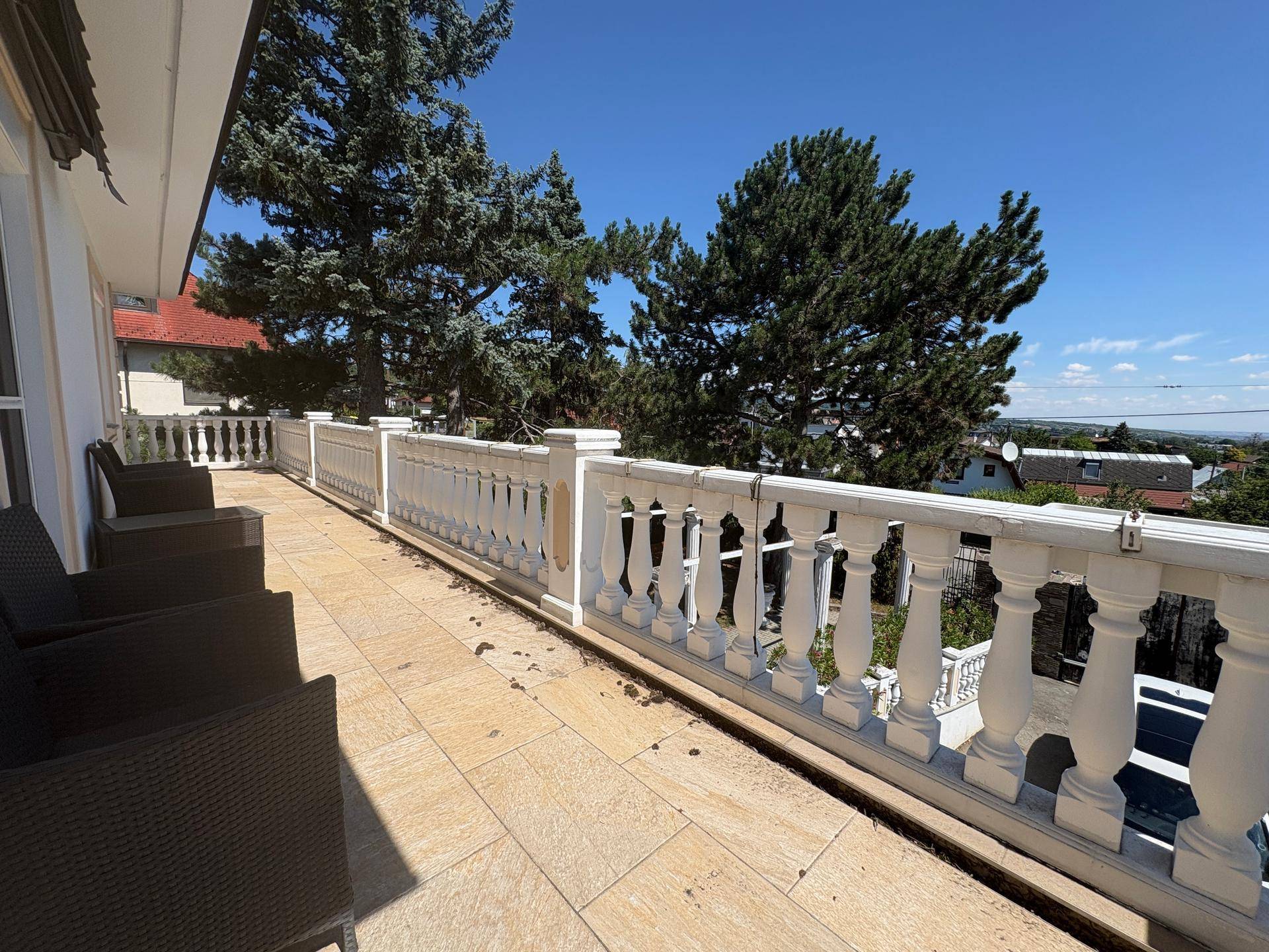 Sonniger Balkon mit bequemen Outdoor-Sitzgelegenheiten und Blick auf die umliegenden Bäume und die Landschaft.