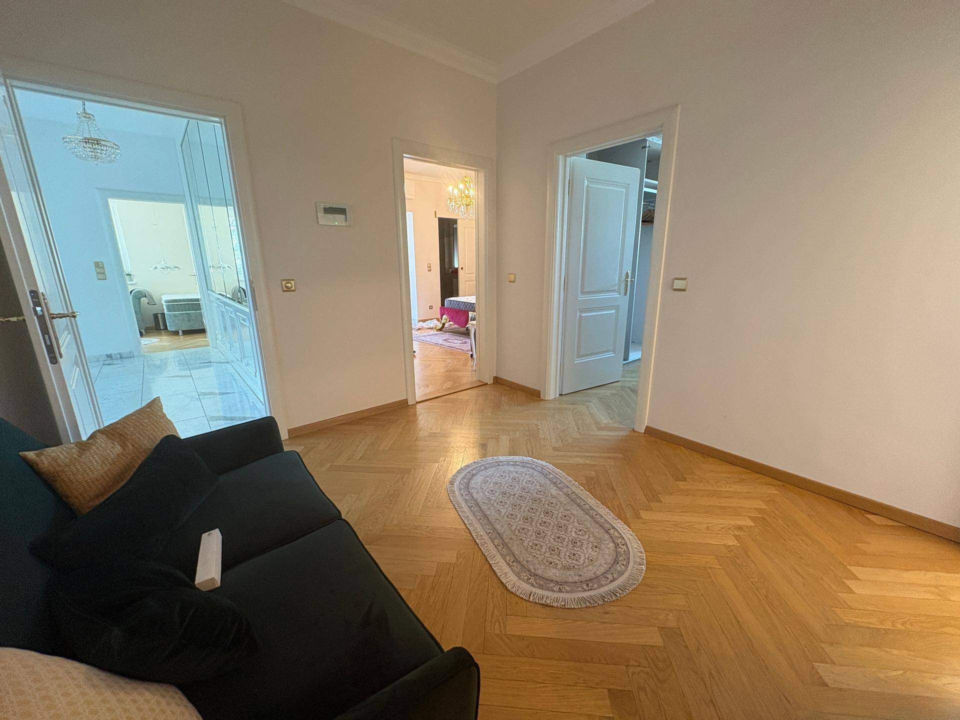 Gemütlicher Wohnbereich mit Sofa und elegantem Fischgrätparkett, der Zugang zu mehreren Zimmern bietet.