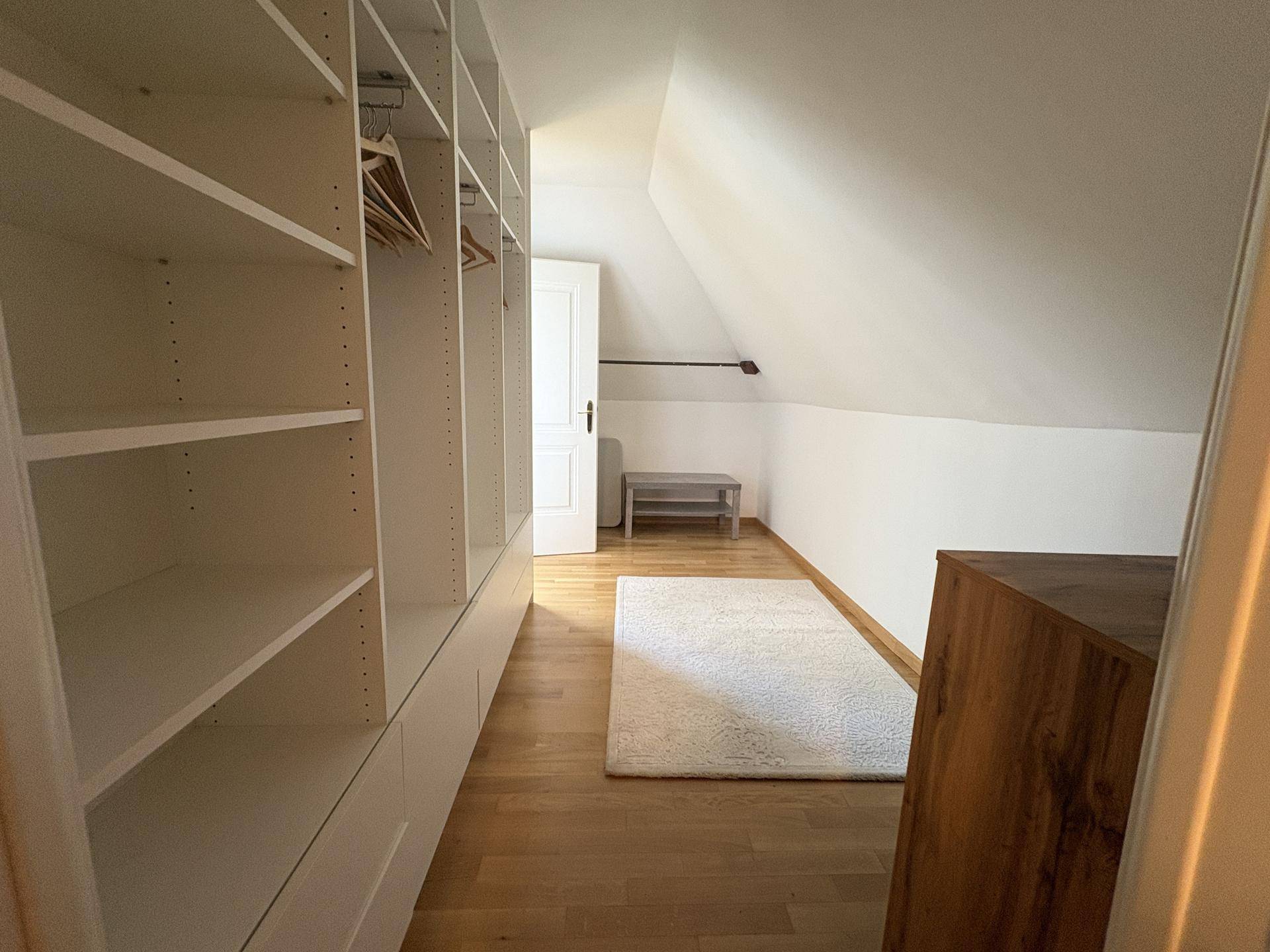 Geräumiger begehbarer Kleiderschrank mit vielen Regalen und Stauraum unter der Dachschräge.