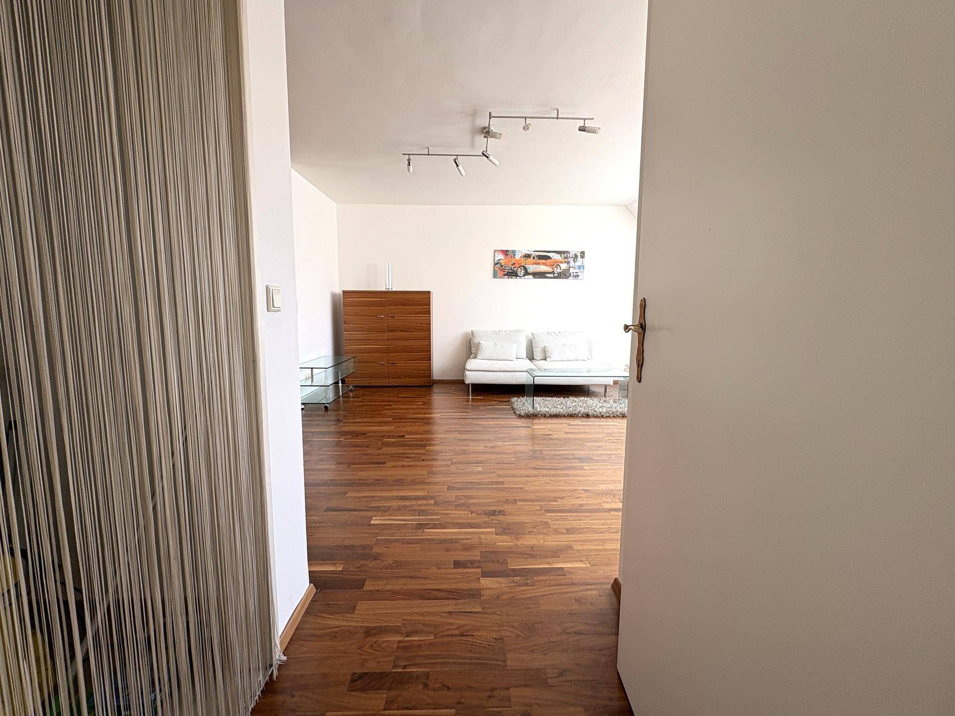 Blick vom Flur in den hellen Wohnbereich mit Holzboden und moderner Einrichtung, durch eine offene Tür.