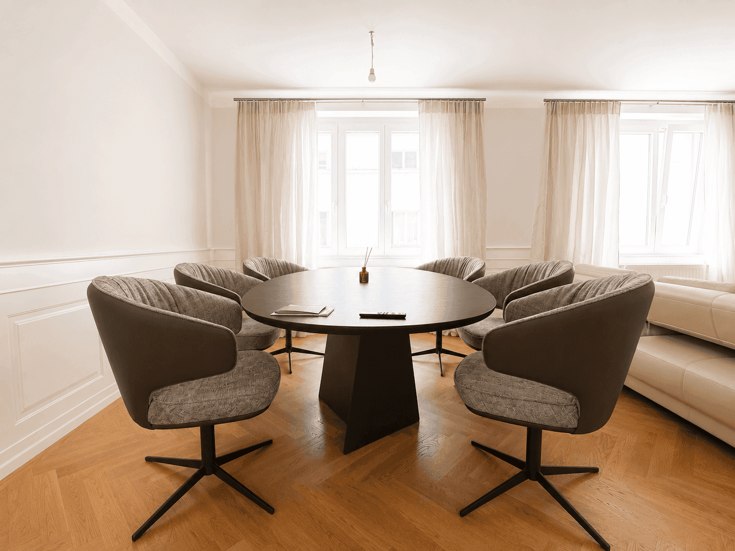 Stilvoller Essbereich mit dunklem Rundtisch, sechs modernen Stühlen und hellem Fischgrätparkett.