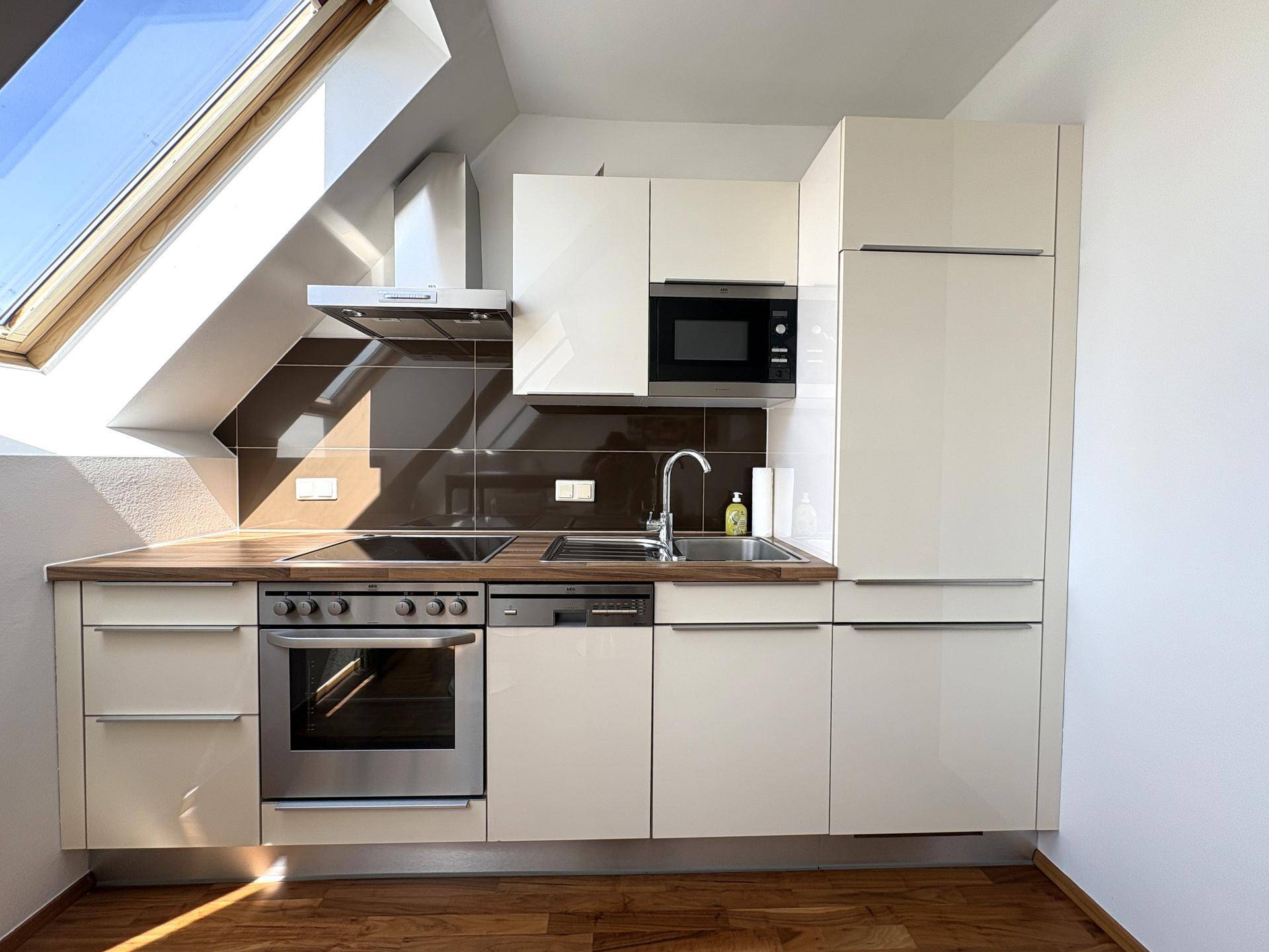 Kompakte, moderne Einbauküche mit integrierten Geräten und Arbeitsplatte aus Holz in heller Ausführung.