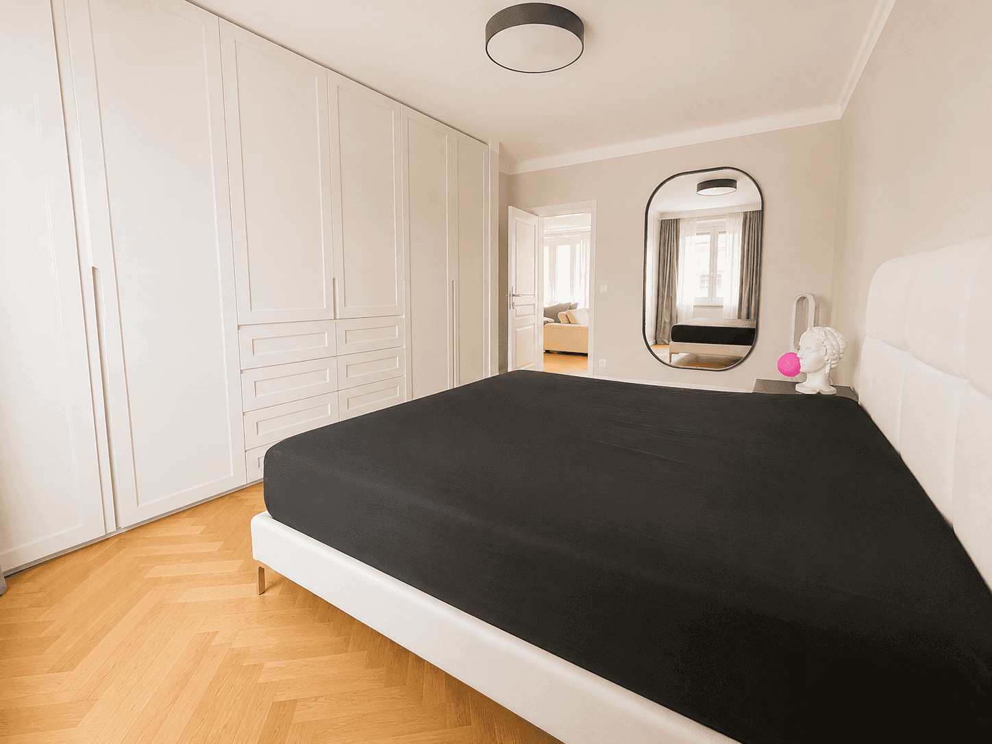 Komfortables Schlafzimmer mit großem Bett, weißen Einbauschränken und Fischgrätparkett.