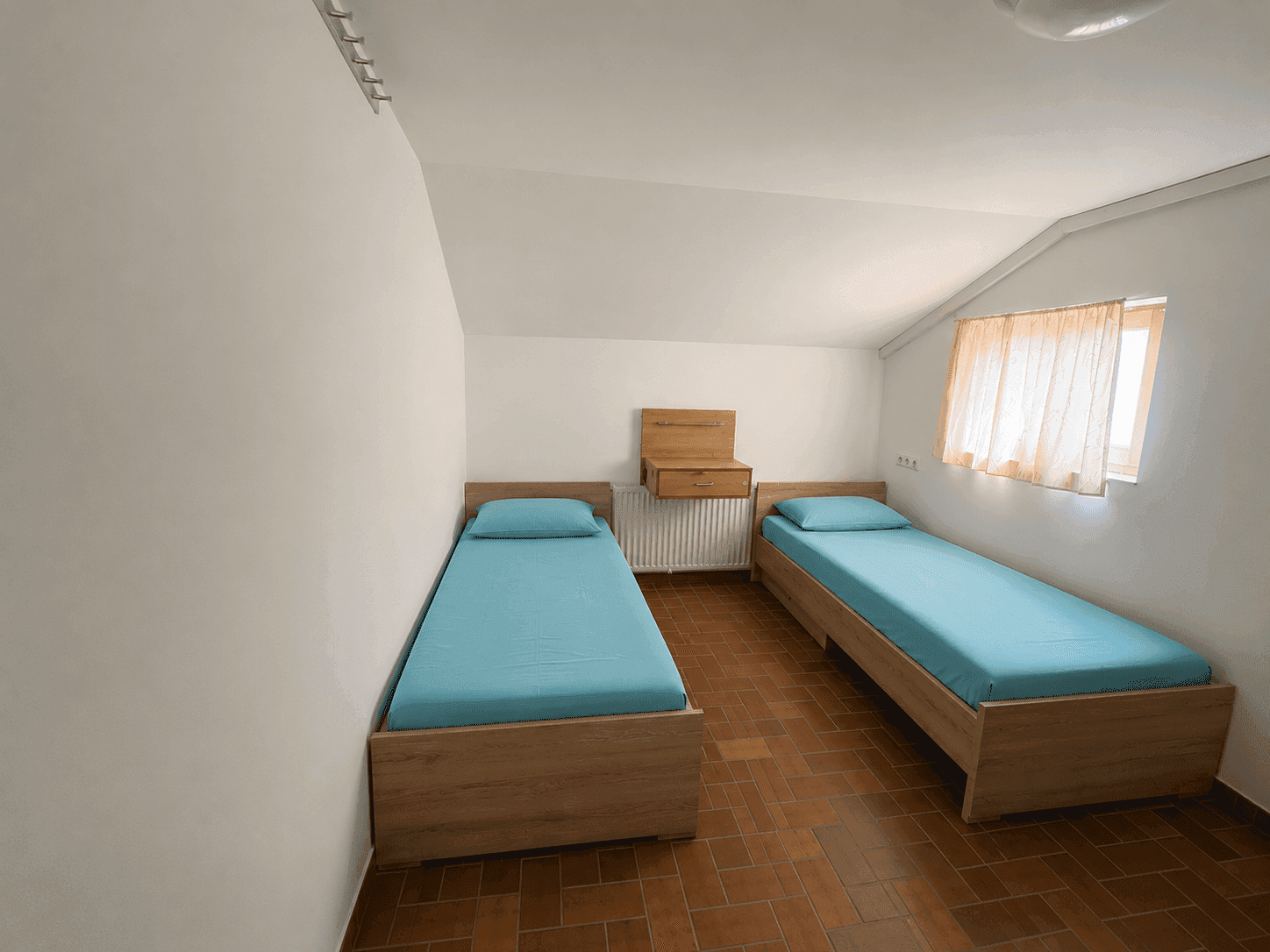 Gemütliches Schlafzimmer mit zwei Einzelbetten, Terrakottafliesen und einem Fenster unter der Dachschräge.