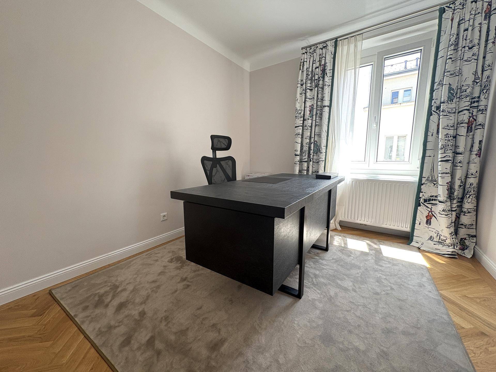 Arbeitszimmer mit großem Schreibtisch, Bürostuhl und Fenster mit dekorativen Vorhängen.