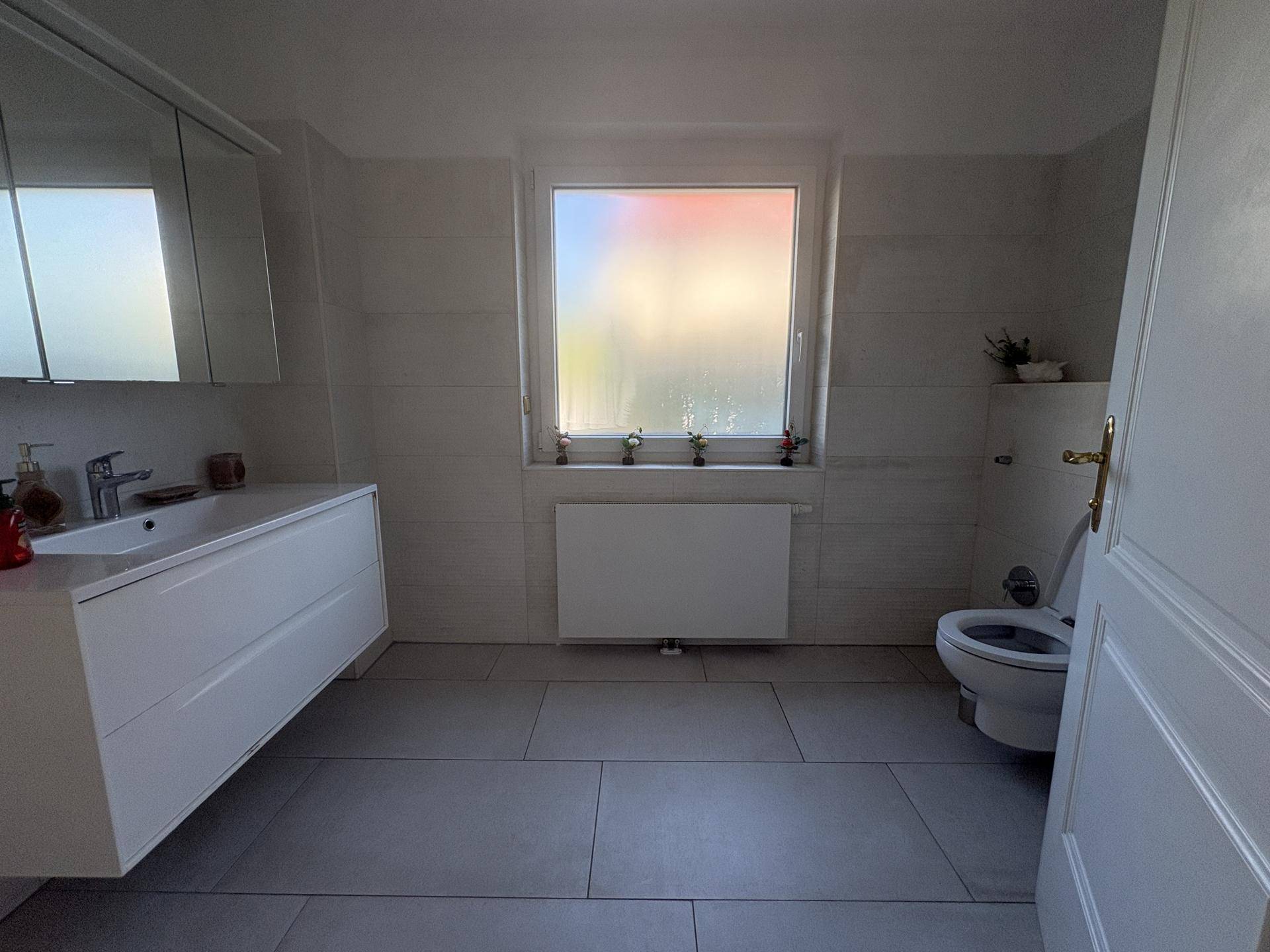 Helles Badezimmer mit Fenster, modernem Waschtisch und Wand-WC.