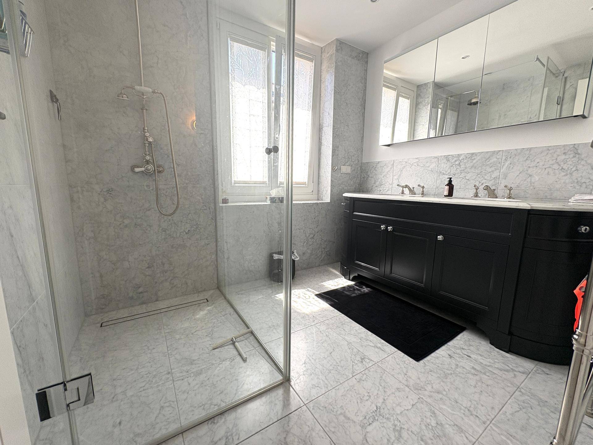 Helles Badezimmer mit Marmorfliesen, großer begehbarer Dusche und Doppelwaschbecken.