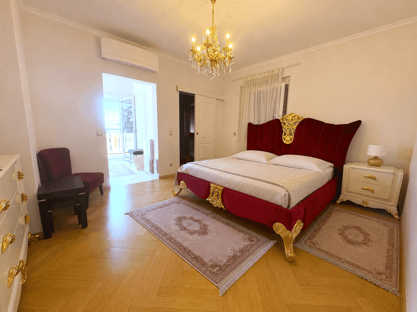Elegantes Schlafzimmer mit rotem Polsterbett, goldenen Akzenten und Fischgrätparkett, ausgestattet mit Klimaanlage.