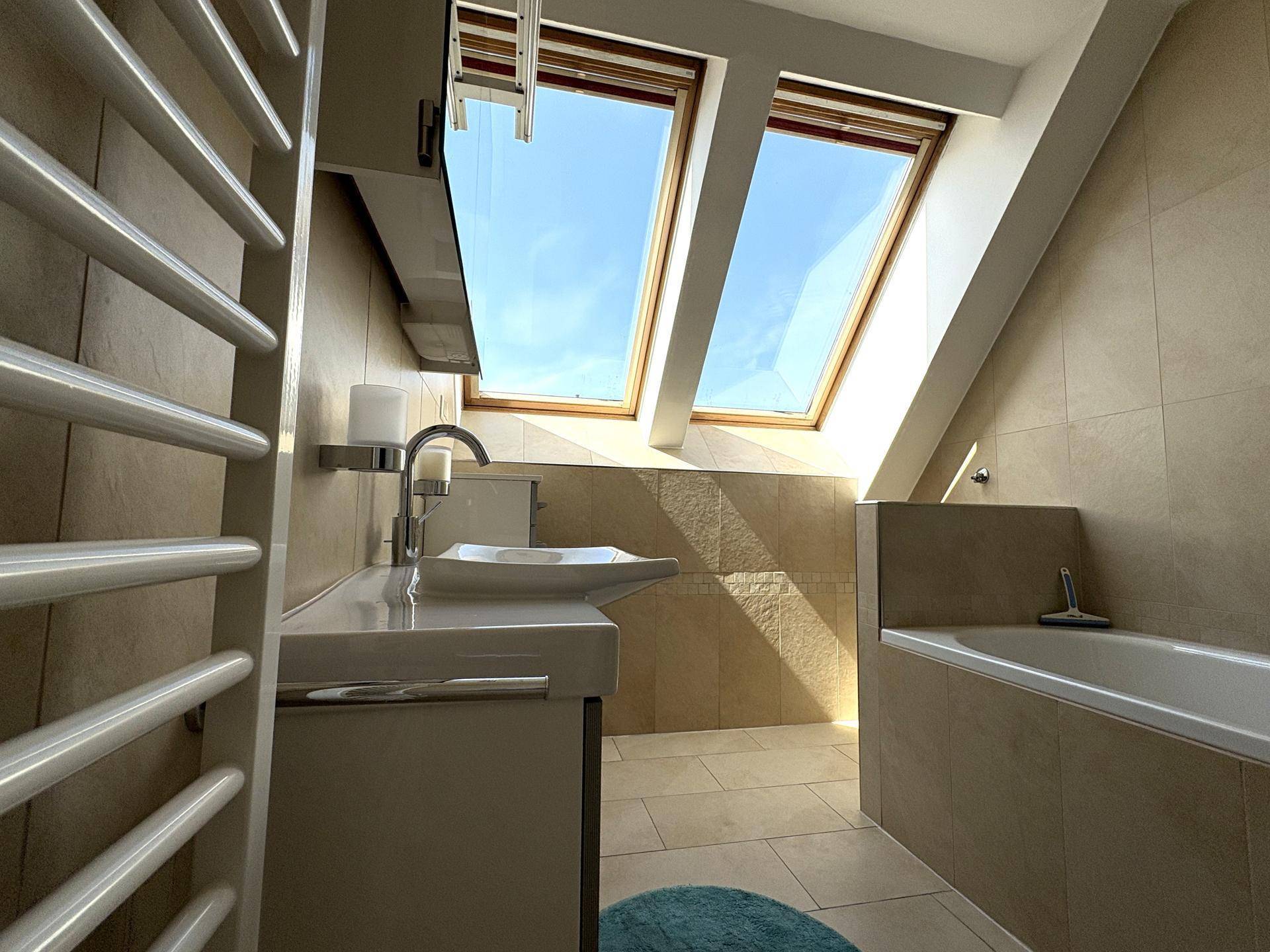 Modernes Badezimmer mit Badewanne, Waschtisch und Dachfenstern für viel Tageslicht unter Schrägdach.