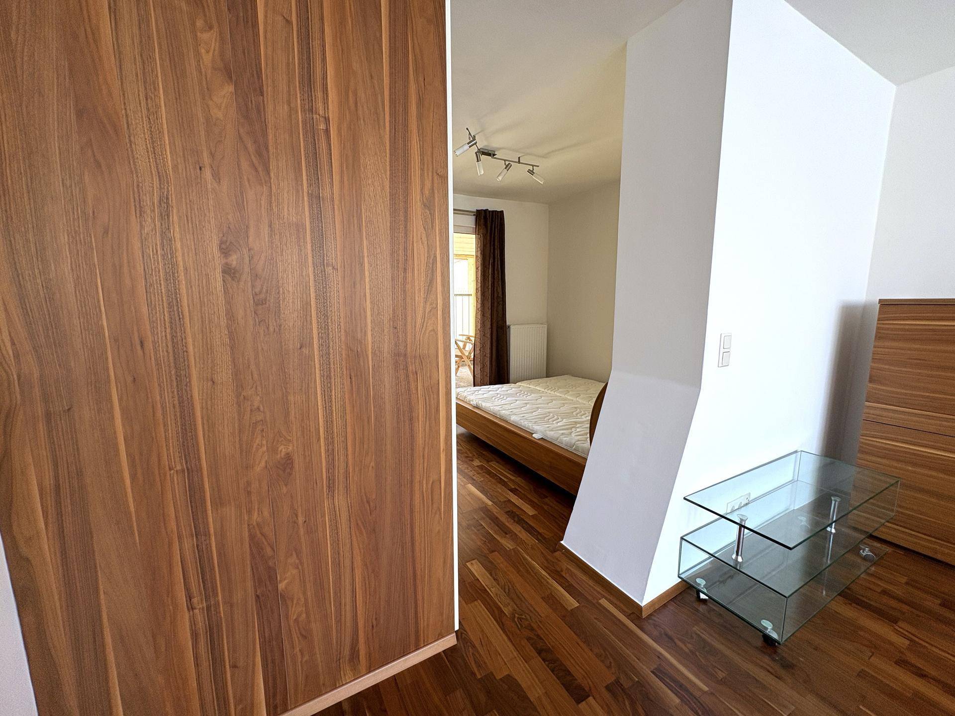 Schlafzimmer mit Holzboden und Blick in den offenen Wohnbereich, bietet eine helle Atmosphäre.