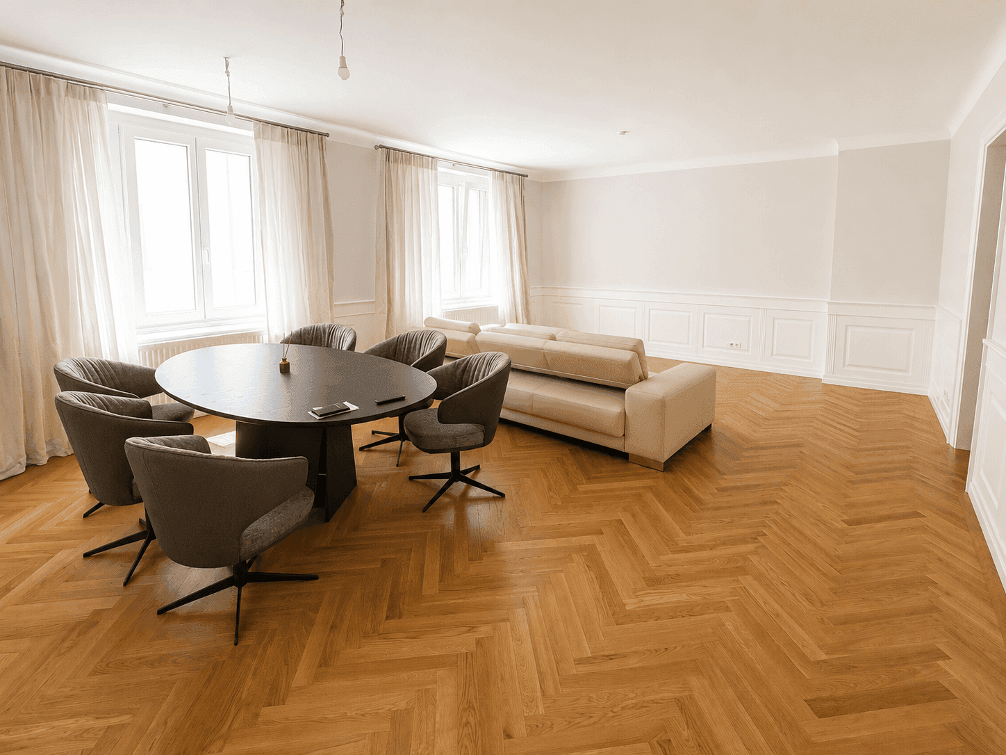Geräumiger Wohn- und Essbereich mit Fischgrätparkett, modernem Esstisch und beigem Sofa.