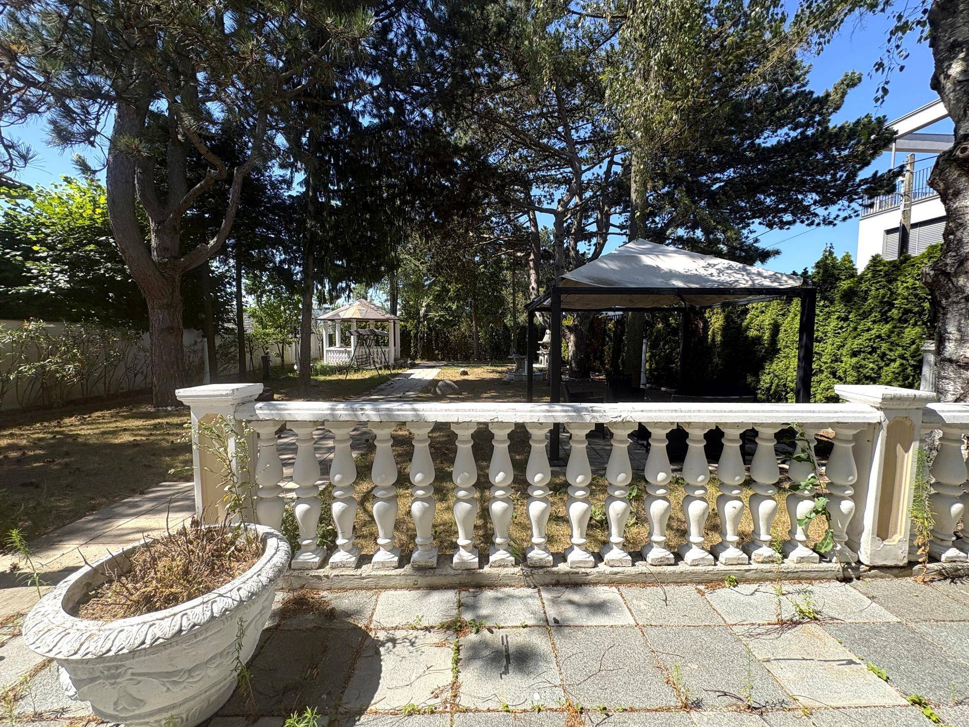 Großer Gartenbereich mit Balustrade, Bäumen und einem Pavillon im Hintergrund.