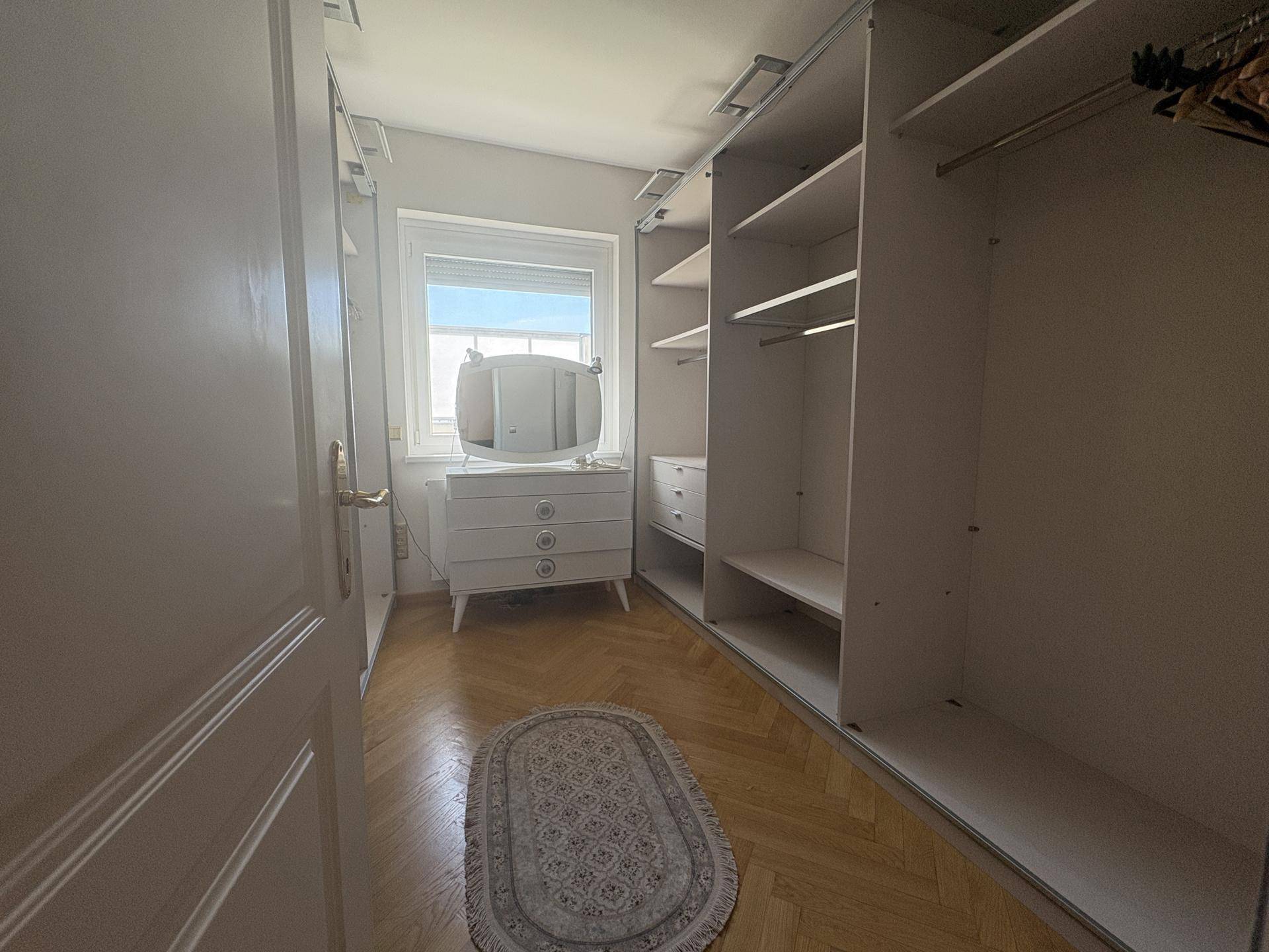 Heller begehbarer Kleiderschrank mit Fenster, integrierten Regalen und einem Schminktisch, bietet viel Stauraum.