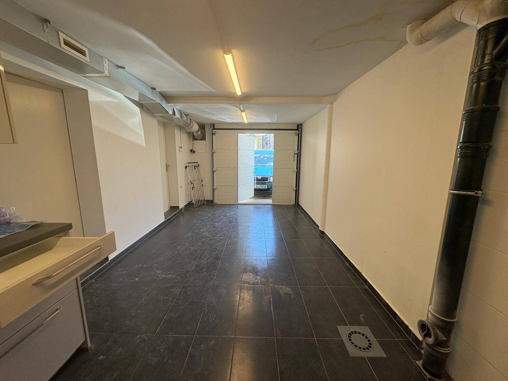 Geräumige Garage mit Fliesenboden und Rolltor, bietet Platz für Fahrzeuge und Lagerung.