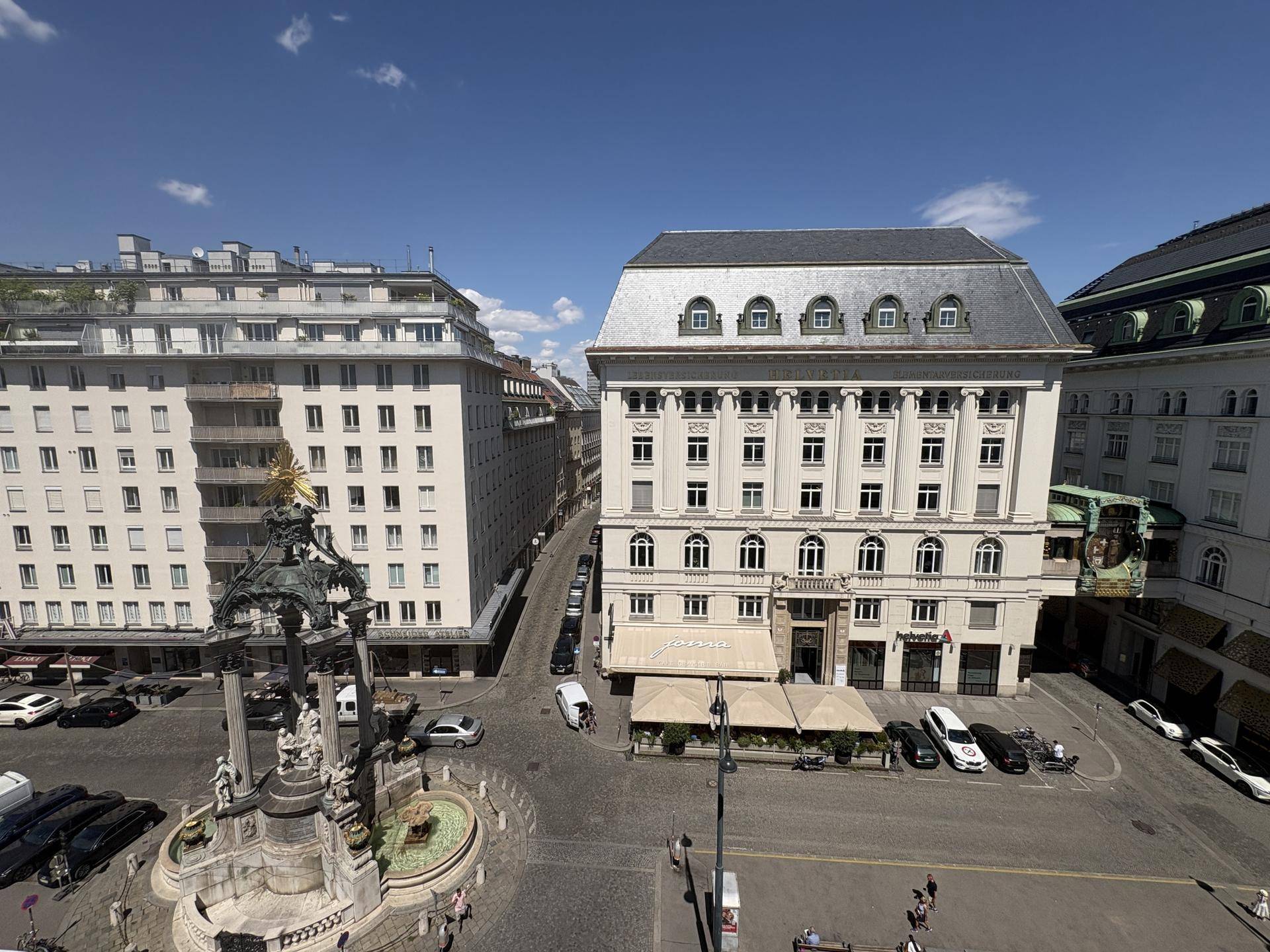 Panoramablick auf einen belebten Stadtplatz mit historischen Gebäuden und einem Denkmal.