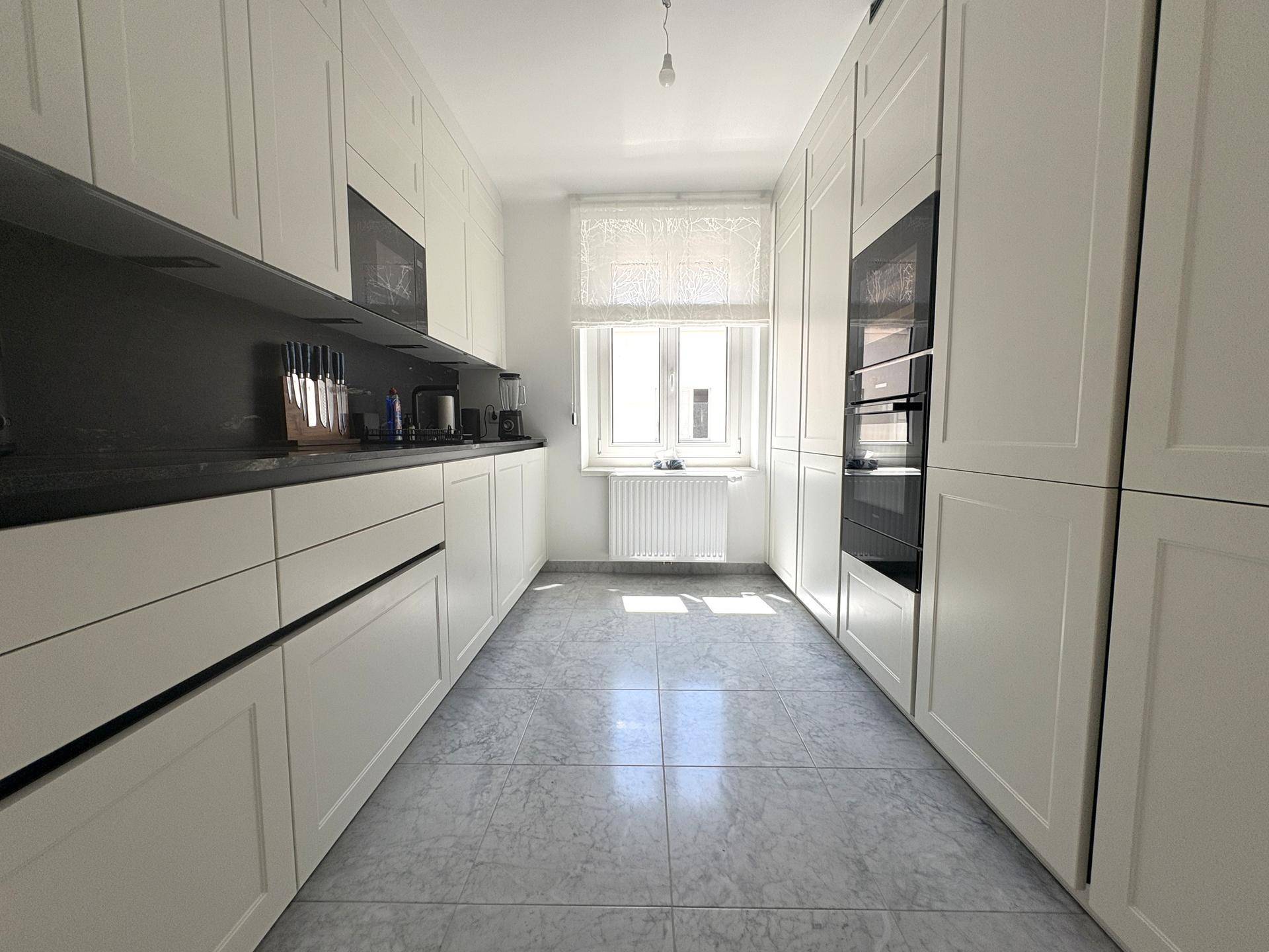 Moderne weiße Küche mit schwarzen Arbeitsplatten, Einbaugeräten und hellem Fliesenboden.
