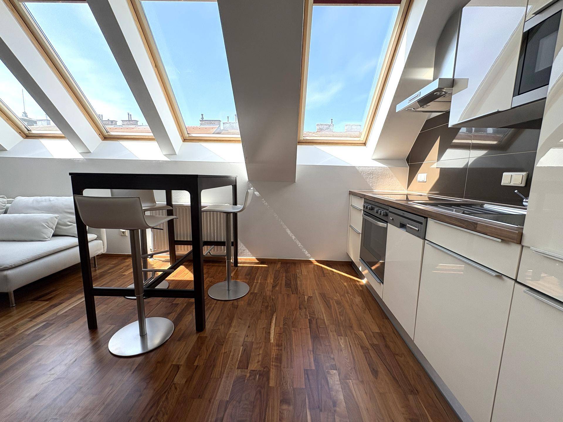 Moderne Einbauküche mit Bar, Dachfenstern und hochwertigen Geräten in hellem Design und Holzoptik.