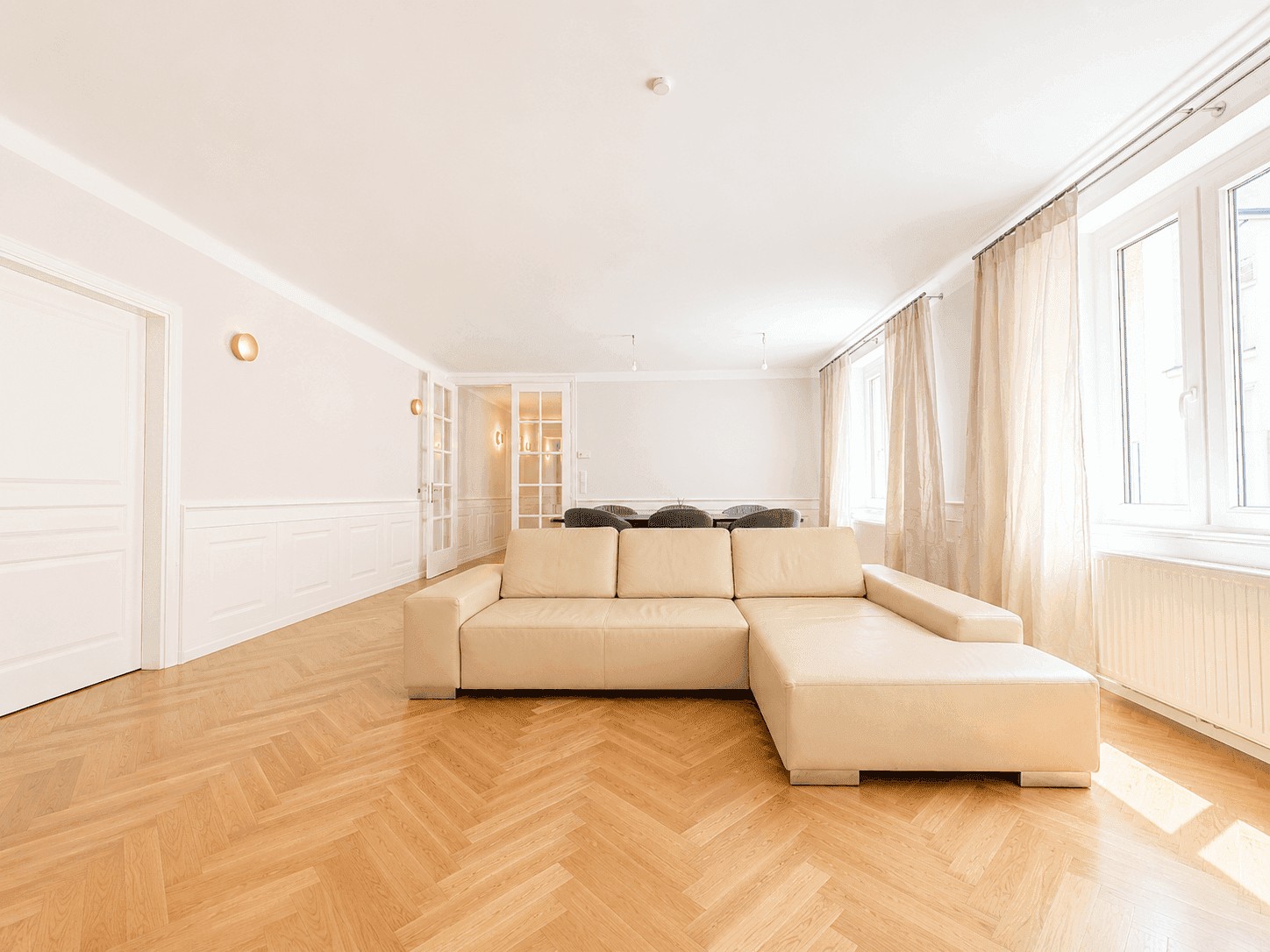Lichtdurchfluteter Wohnbereich mit beigem Sofa, Fischgrätparkett und dekorativen Wandpaneelen.