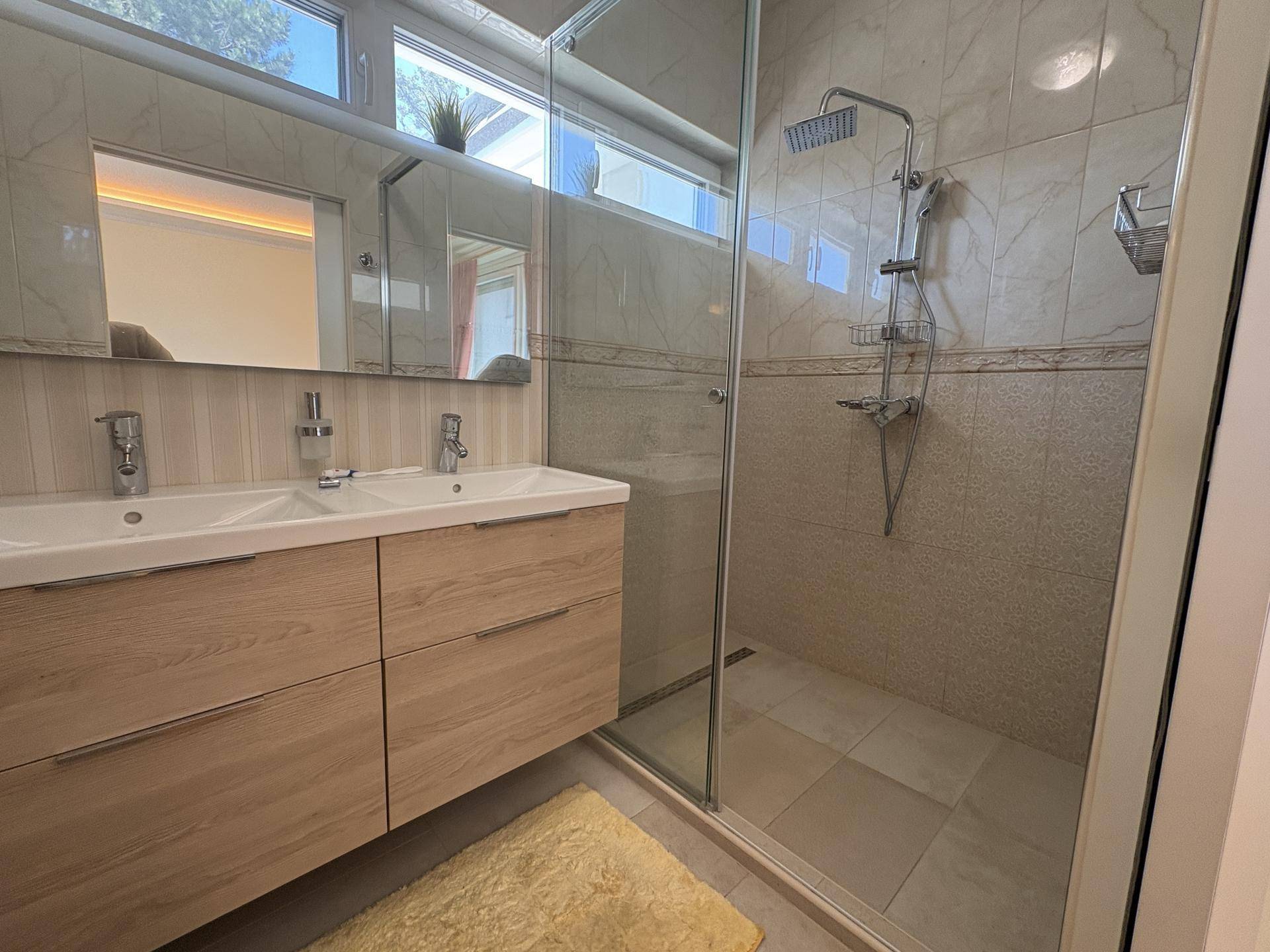Modernes Badezimmer mit Doppelwaschbecken, großem Spiegel und begehbarer Dusche, ausgestattet mit hellen Fliesen.