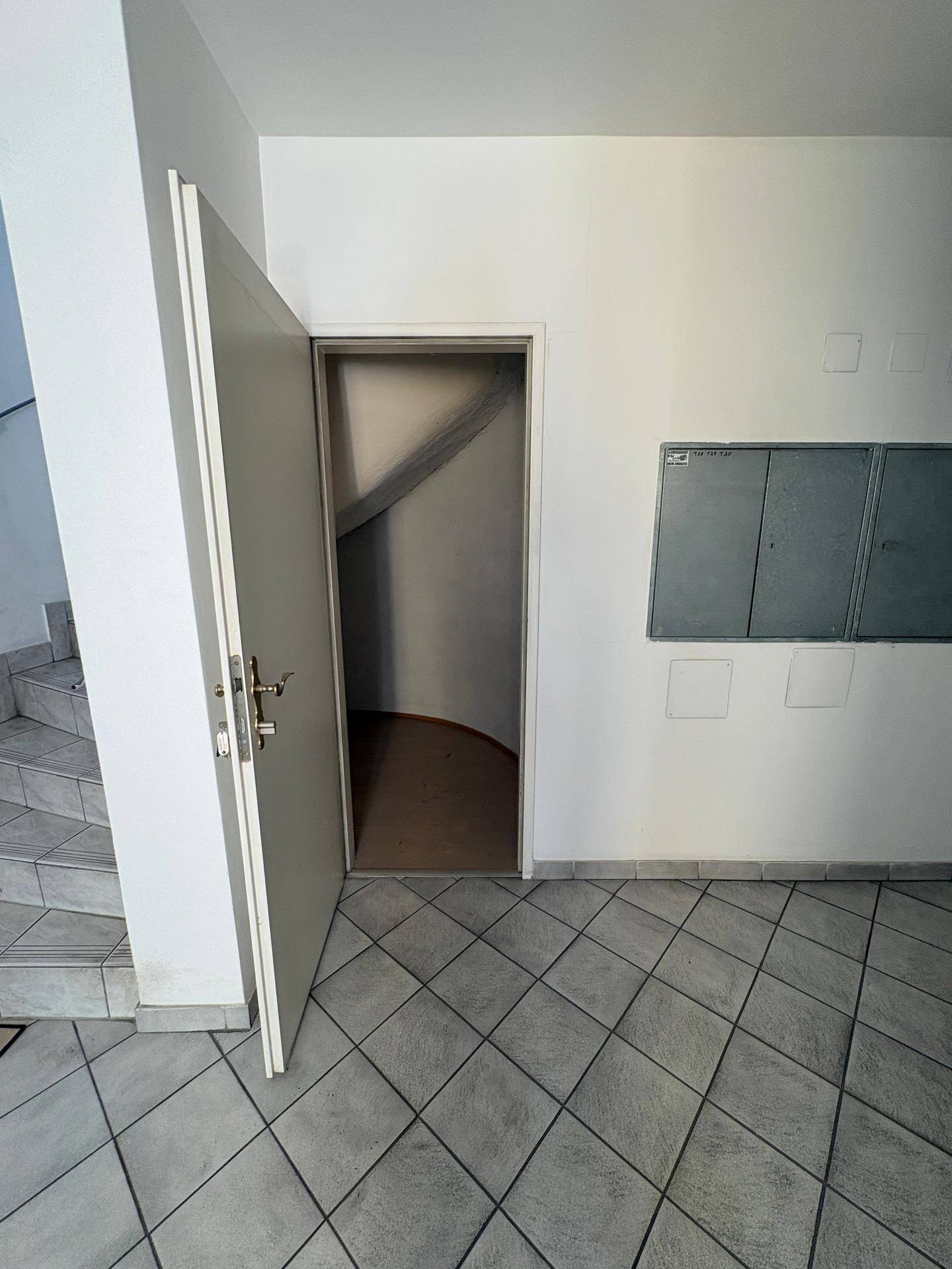 Gemeinschaftlicher Flur mit Fliesenboden und Zugang zu einem Abstellraum unter der Treppe.