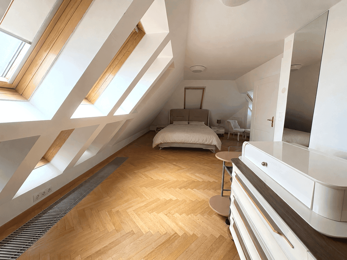 Helles Schlafzimmer im Dachgeschoss mit mehreren Dachfenstern, Fischgrätparkett und gemütlichem Bett.