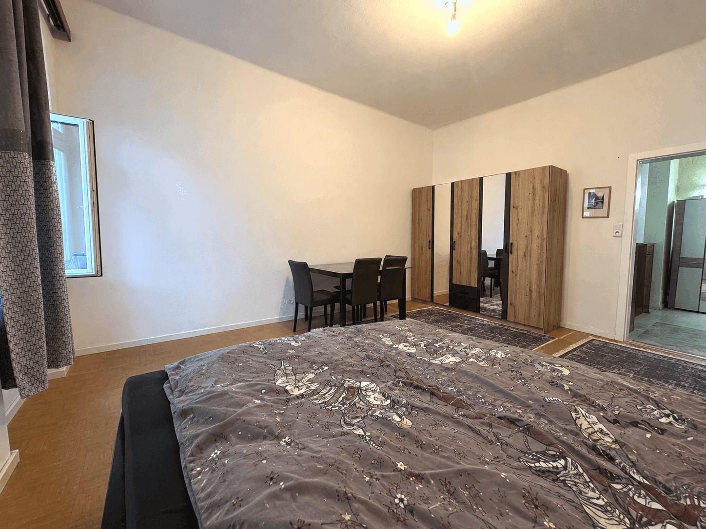 Schlafzimmer mit Doppelbett, Esstisch und großem Kleiderschrank, der den Raum funktional aufteilt.