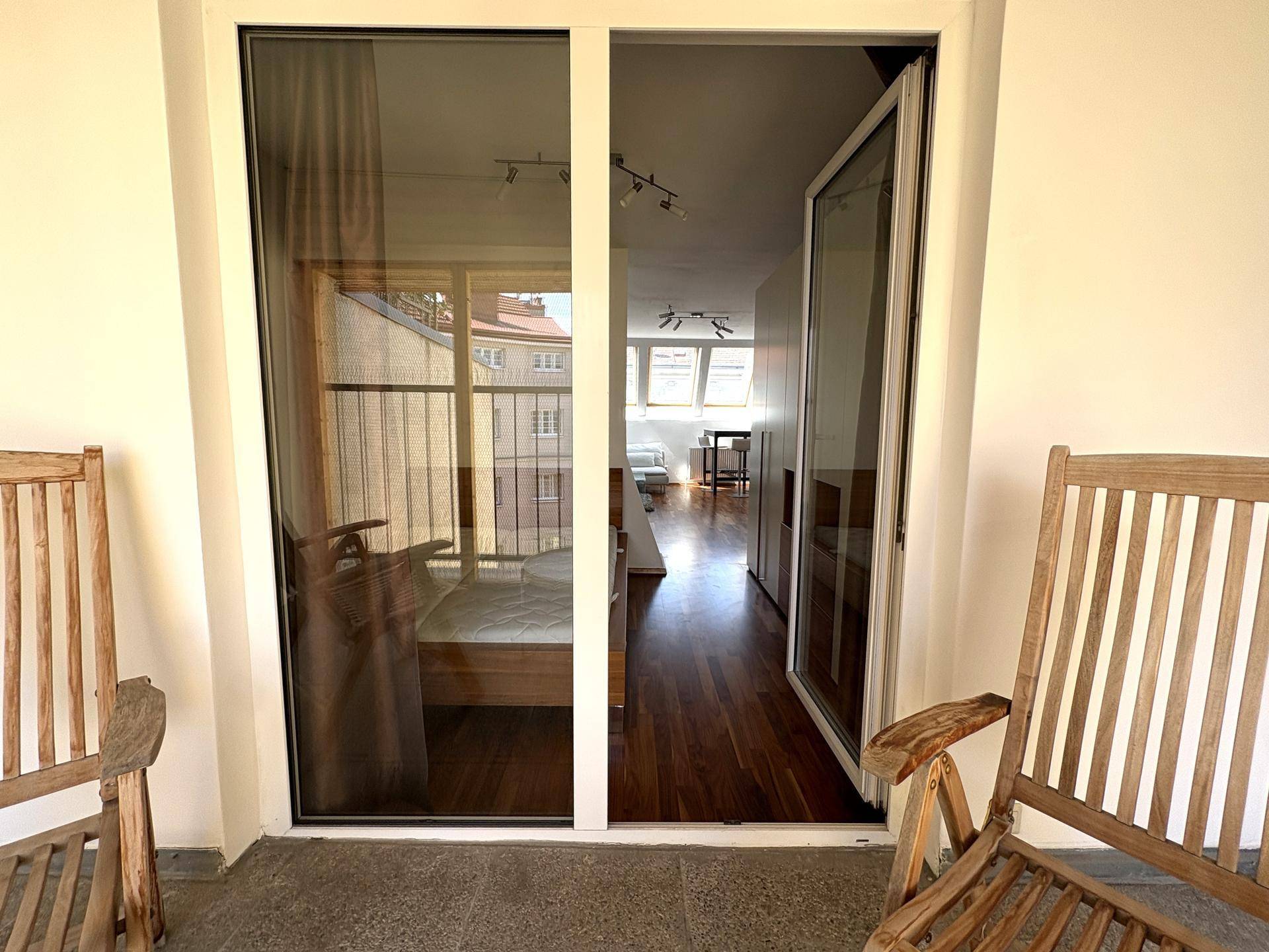 Balkon mit Holzsitzmöbeln und direktem Zugang zum Schlafzimmer, einladend und sonnig.