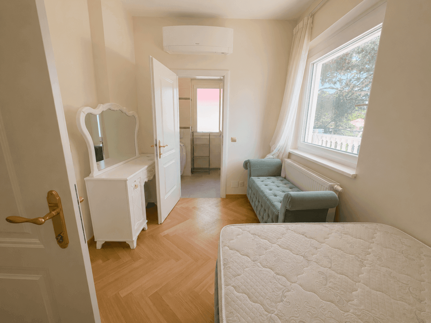 Helles Schlafzimmer mit Schminktisch, Klimaanlage und Fenster, das viel Tageslicht hereinlässt.