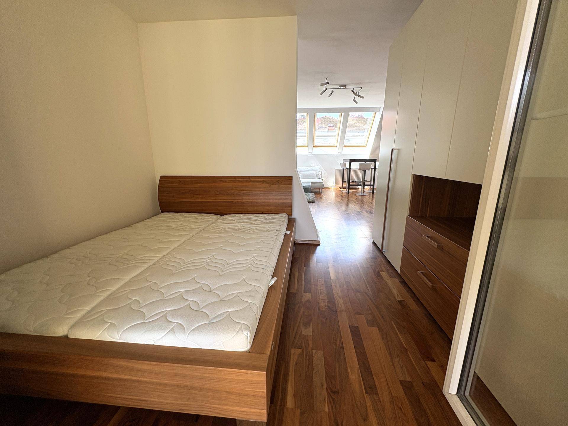 Schlafzimmer mit Holzboden, Einbauschränken und offenem Übergang zum Wohnbereich, modern eingerichtet.