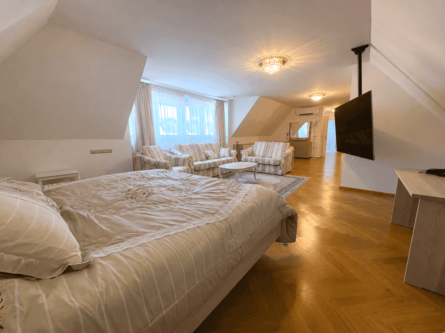 Geräumiges Schlafzimmer im Dachgeschoss mit großem Bett, Sitzbereich und an der Wand montiertem Fernseher.