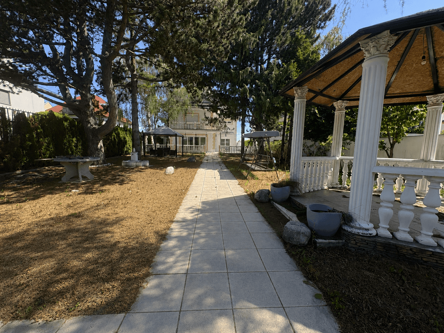 Großer Garten mit Wegen, Bäumen und einem Pavillon im Hintergrund.