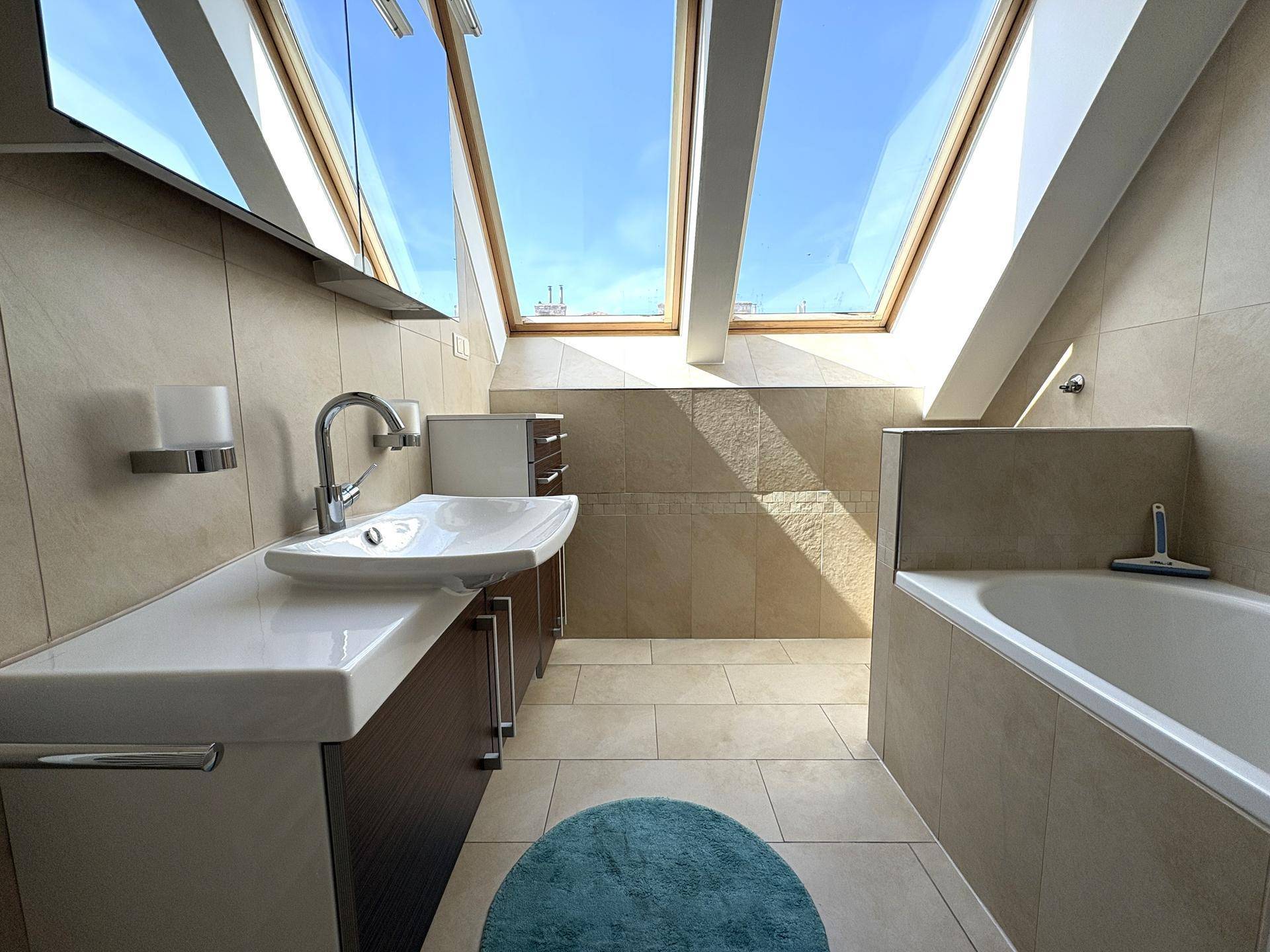 Modernes Badezimmer mit Badewanne, Waschtisch und Dachfenstern für viel Tageslicht unter Schrägdach.