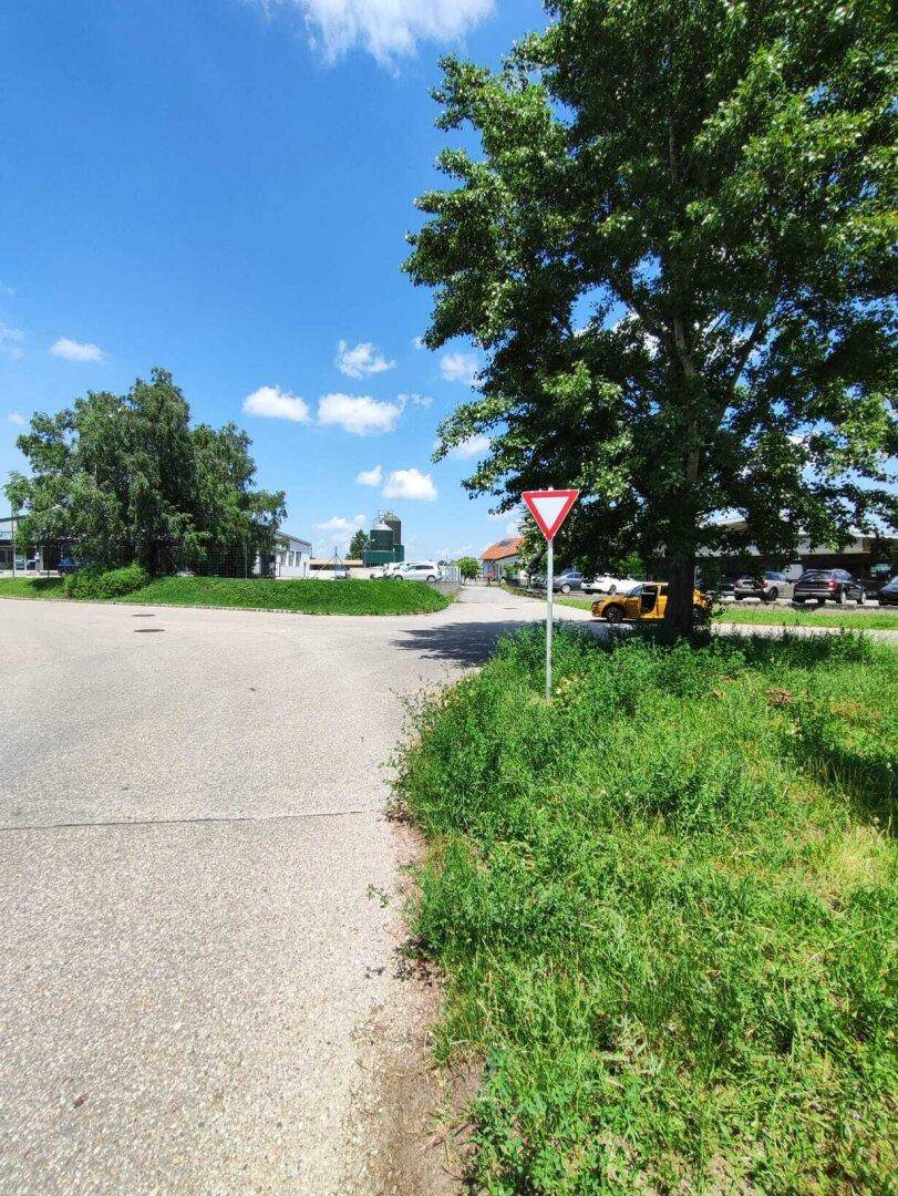 Eine ländliche Straße führt an einem unbebauten Grundstück vorbei, mit gewerblichen Gebäuden in der Ferne.