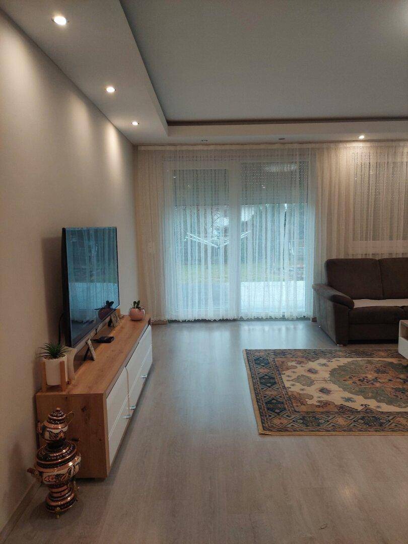 Wohnbereich mit Fernseher, Sideboard und großen Fenstern mit Zugang nach draußen.