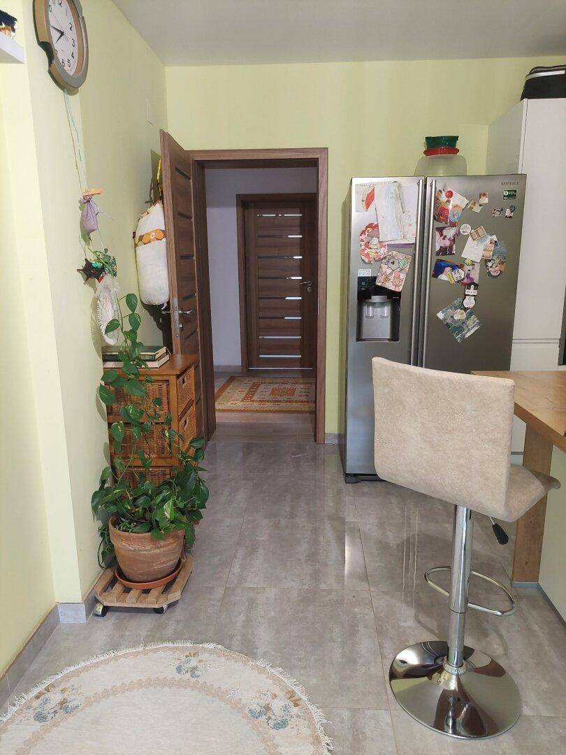 Küchenbereich mit Kühlschrank, Barhocker und Zugang zu einem weiteren Raum.