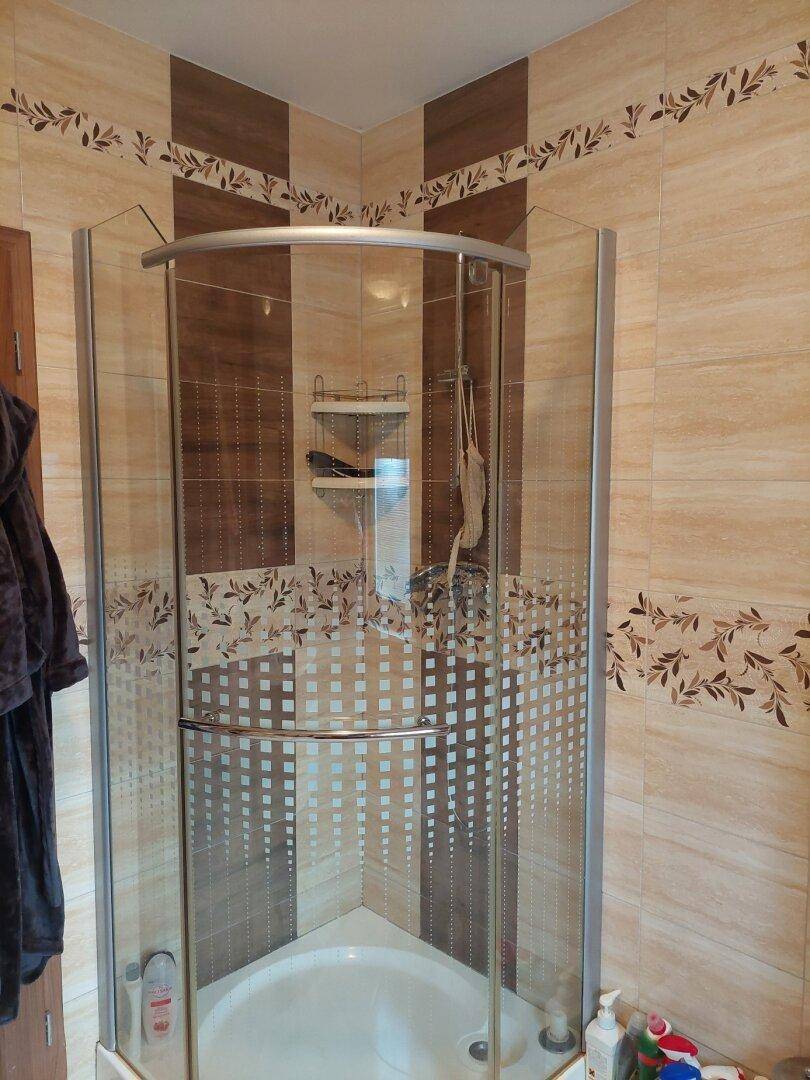 Badezimmer mit Eckdusche, gemusterten Fliesen und praktischen Ablagen.