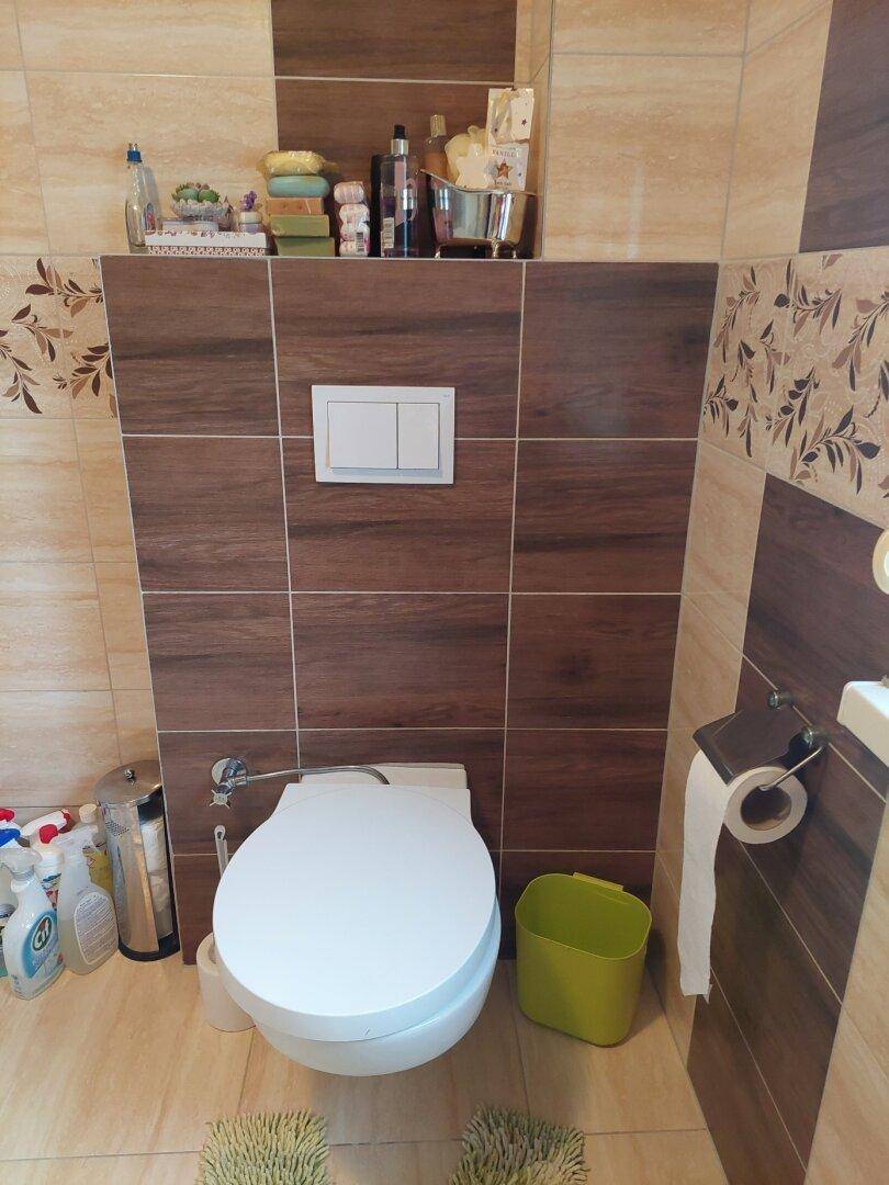 Badezimmer mit wandhängendem WC, modernen Fliesen und praktischem Stauraum.
