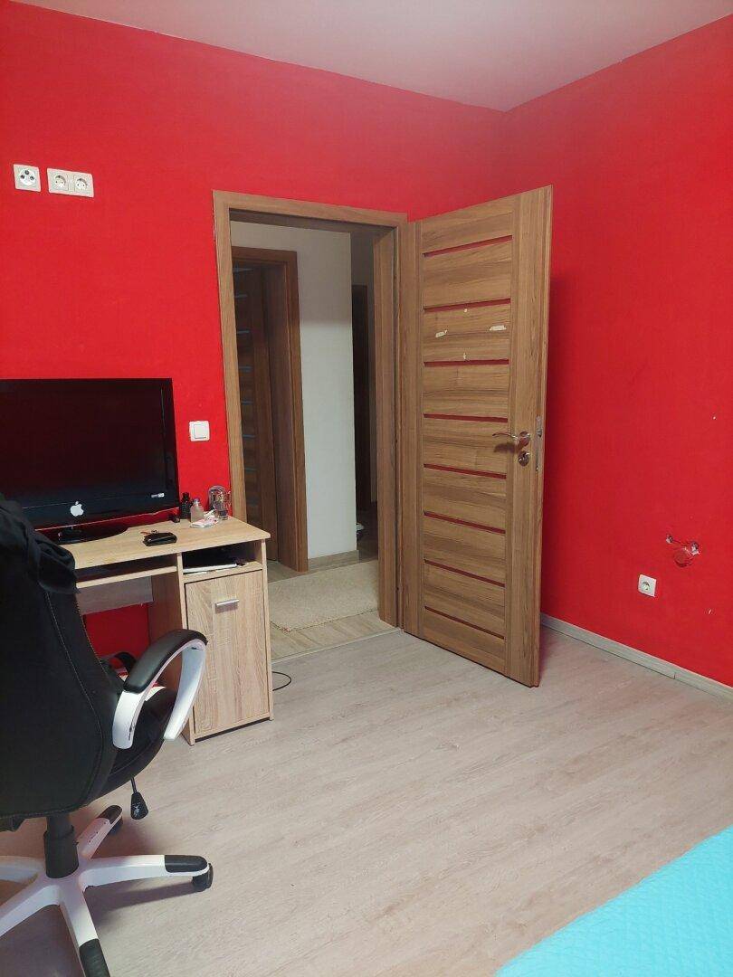 Zimmer mit leuchtend roten Wänden, Schreibtisch und Holztür.