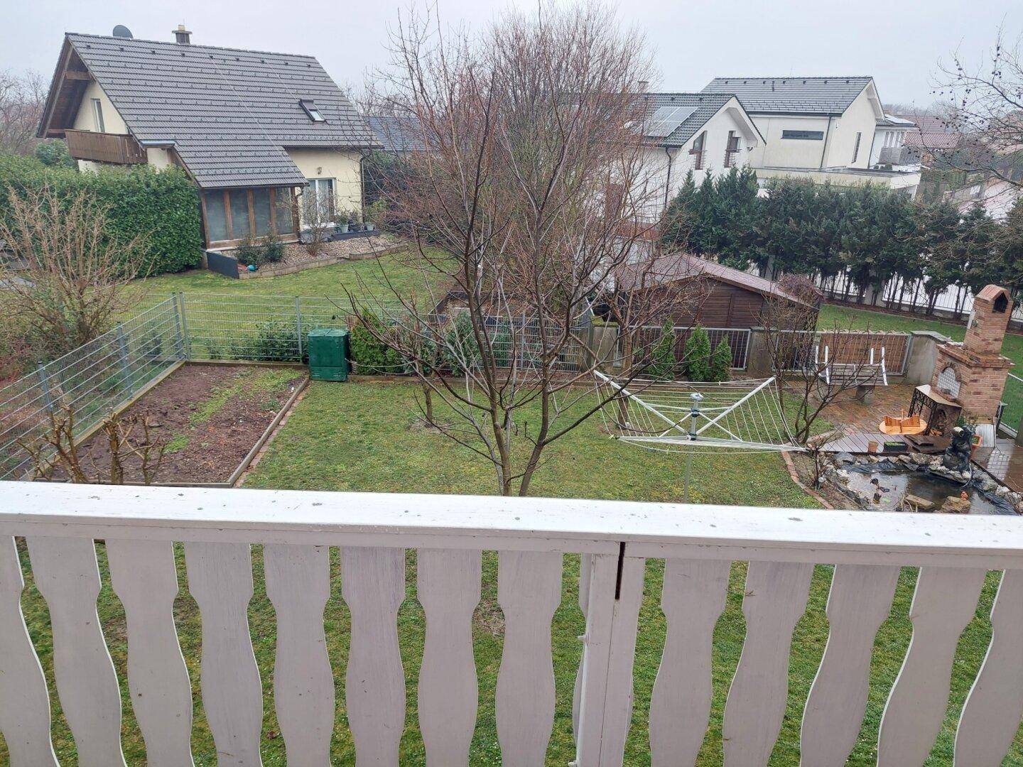 Blick vom Balkon auf den Garten mit Rasenfläche, Teich und gemauertem Grill.