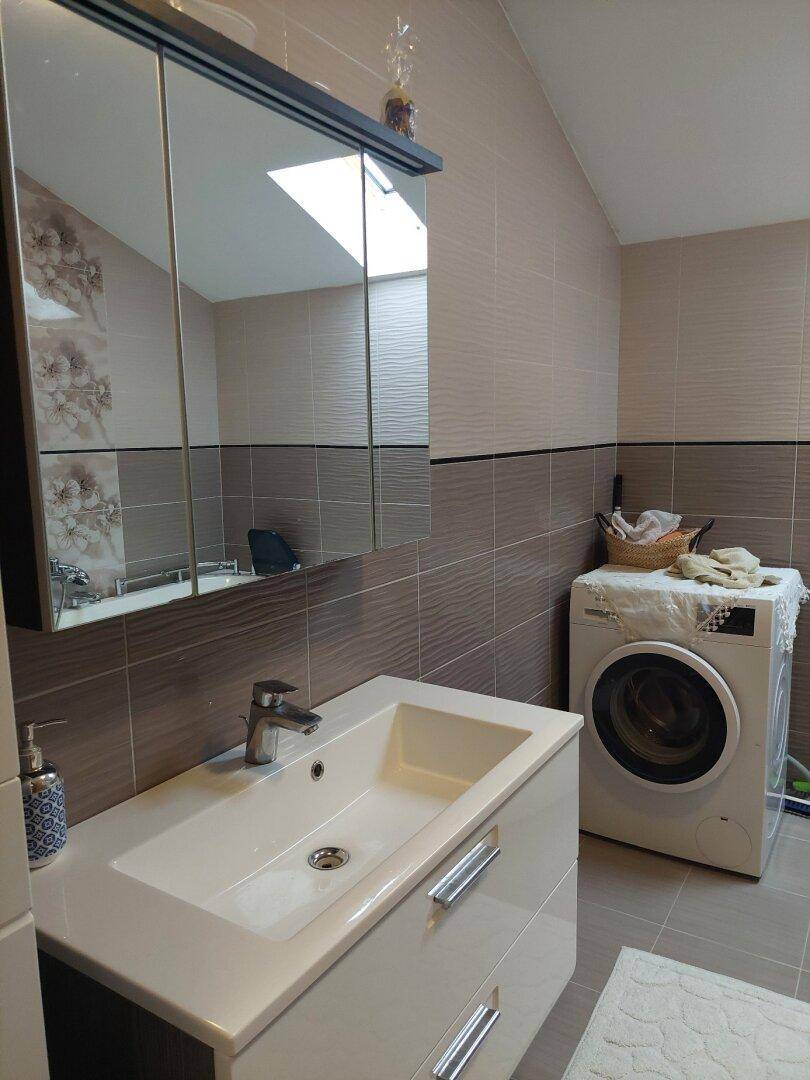Badezimmer mit Waschbecken, Spiegelschrank und Waschmaschine unter dem Dachfenster.