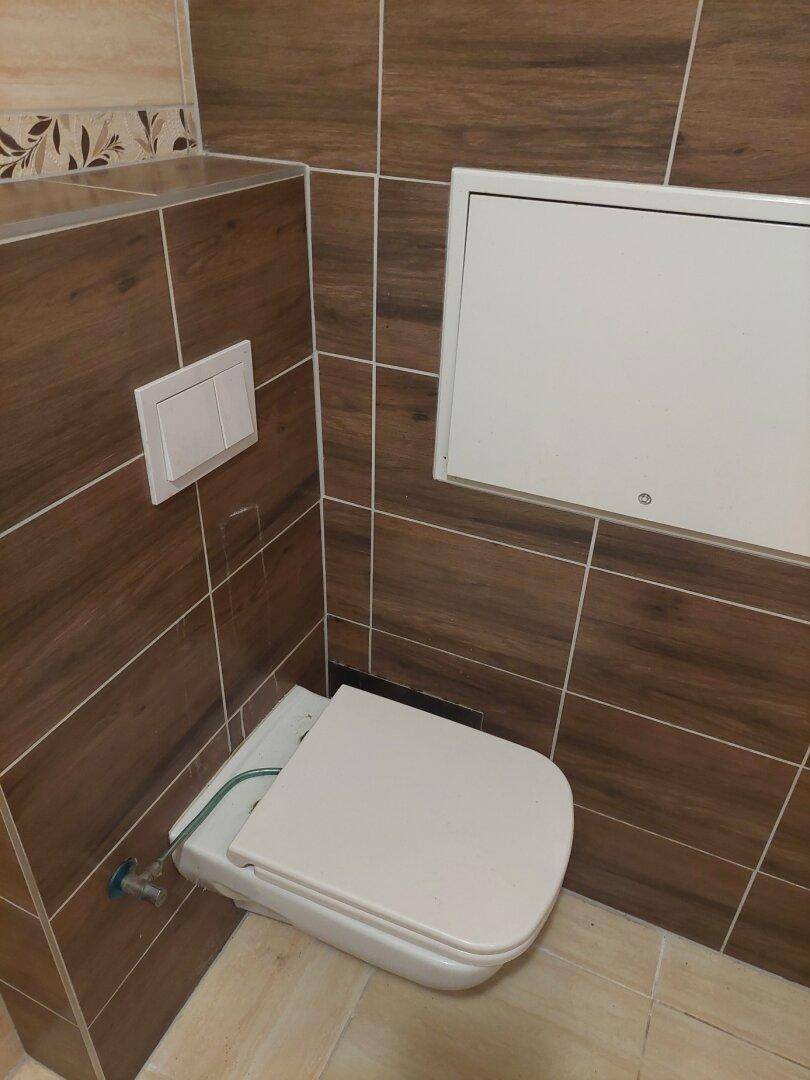 WC mit wandhängender Toilette und braunen Fliesen, inklusive Revisionsklappe.